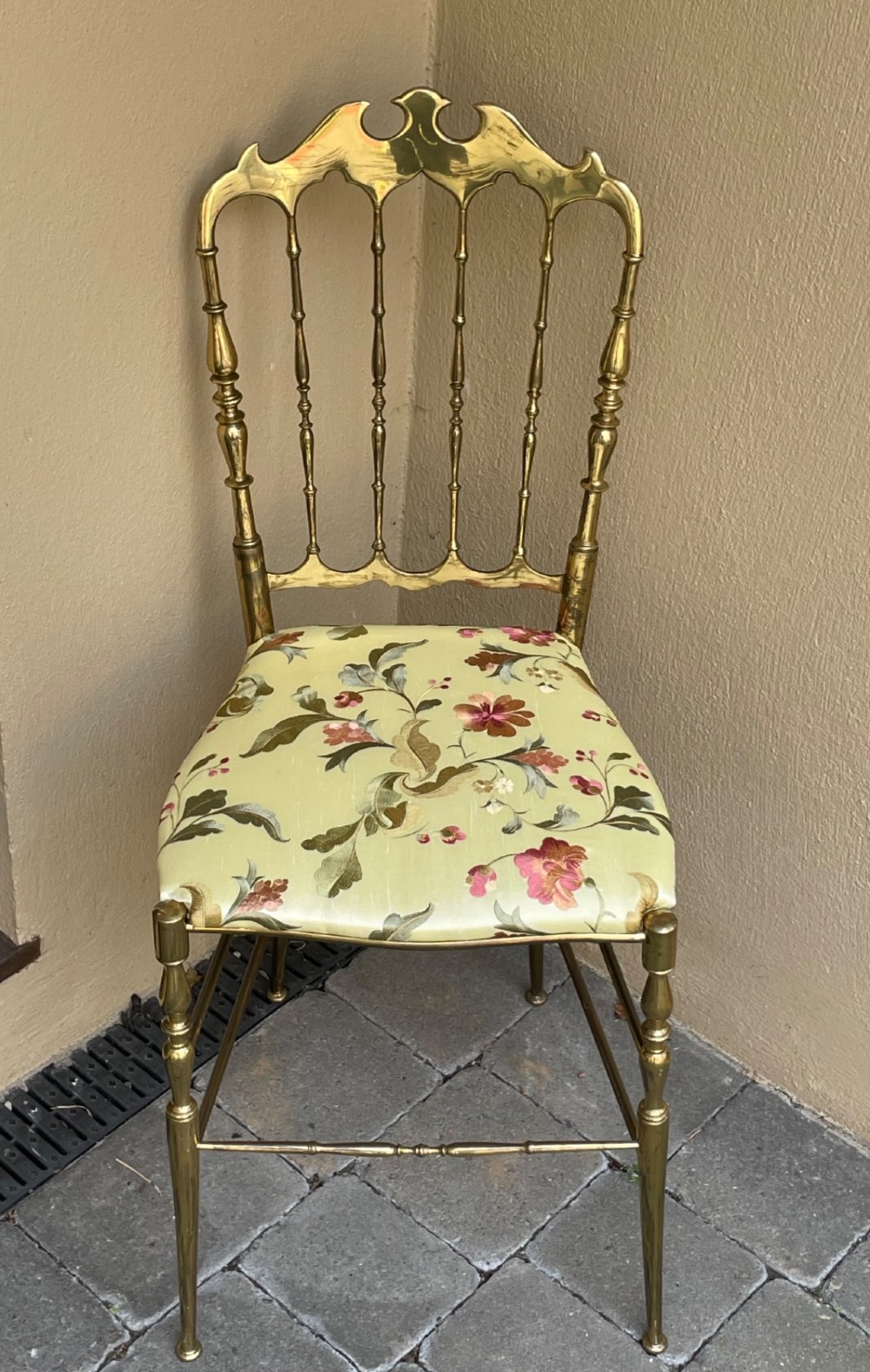 A polished brass Chiavari style salon chair featuring a spindle backrest, ornate cresting rail, turned legs, and a floral upholstered seat. View IV