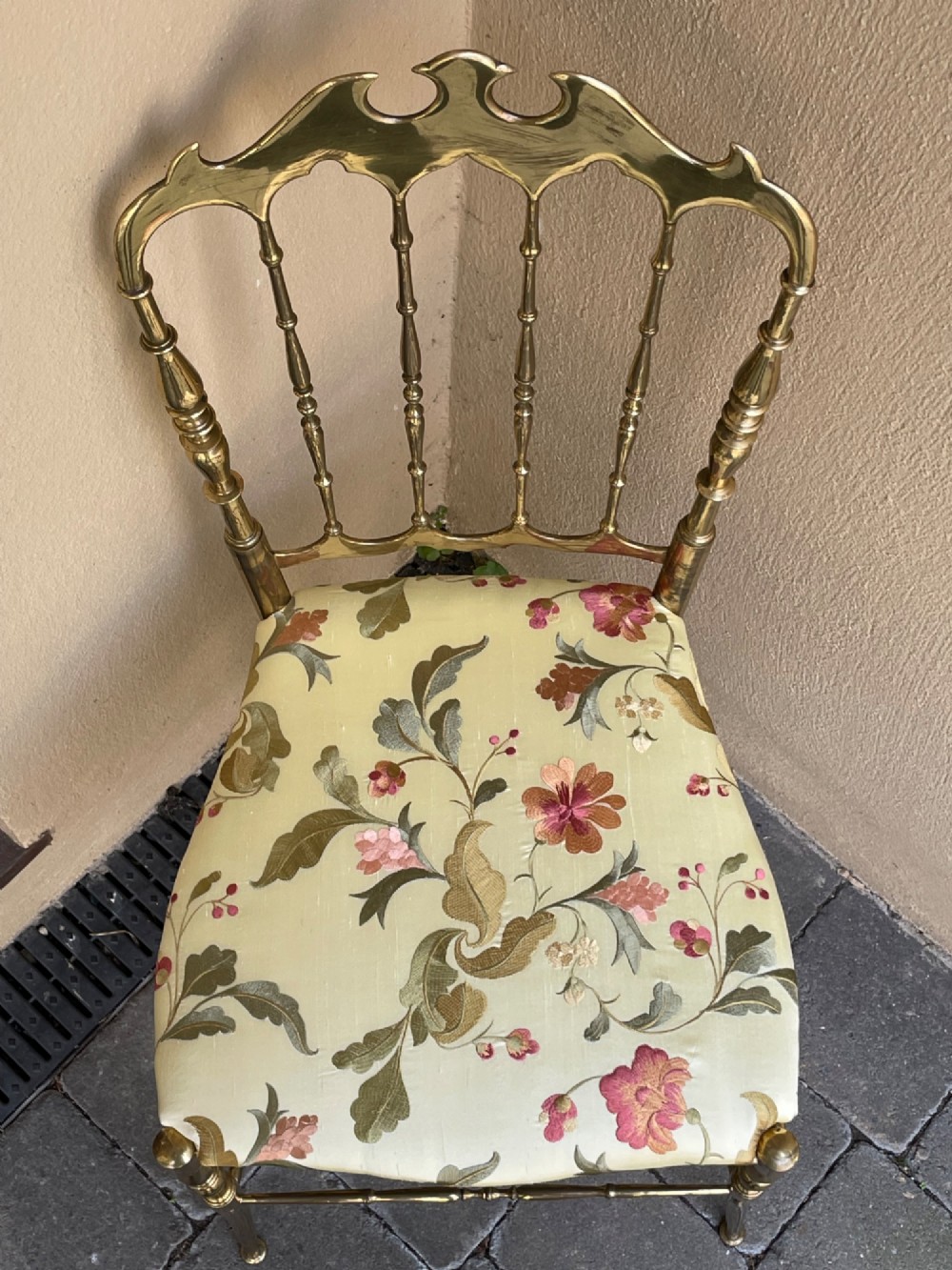 A polished brass Chiavari style salon chair featuring a spindle backrest, ornate cresting rail, turned legs, and a floral upholstered seat. View V