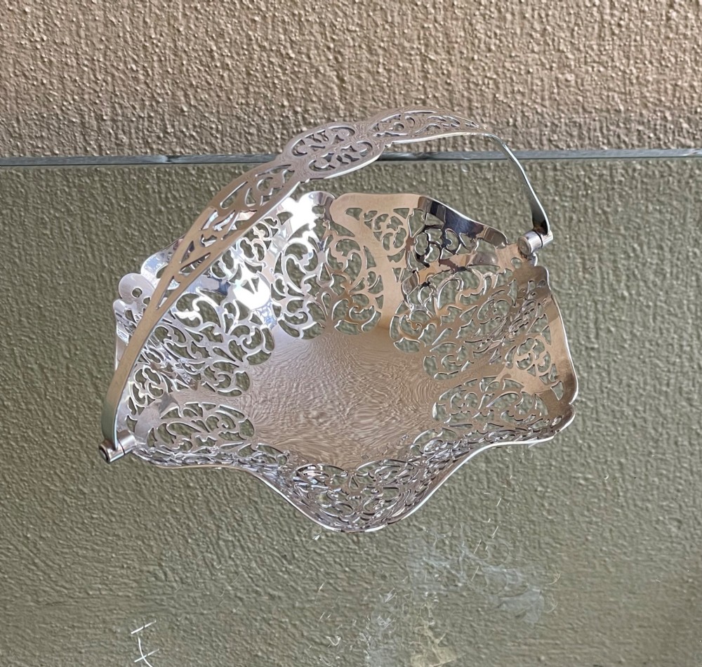 A pierced silver bonbon dish featuring a hinged overhead swing handle and intricate floral lattice openwork. View IV