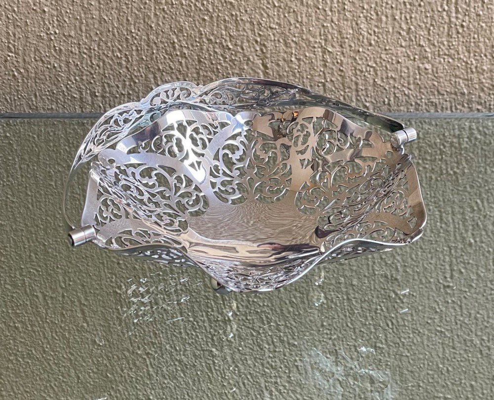 A pierced silver bonbon dish featuring a hinged overhead swing handle and intricate floral lattice openwork. View V