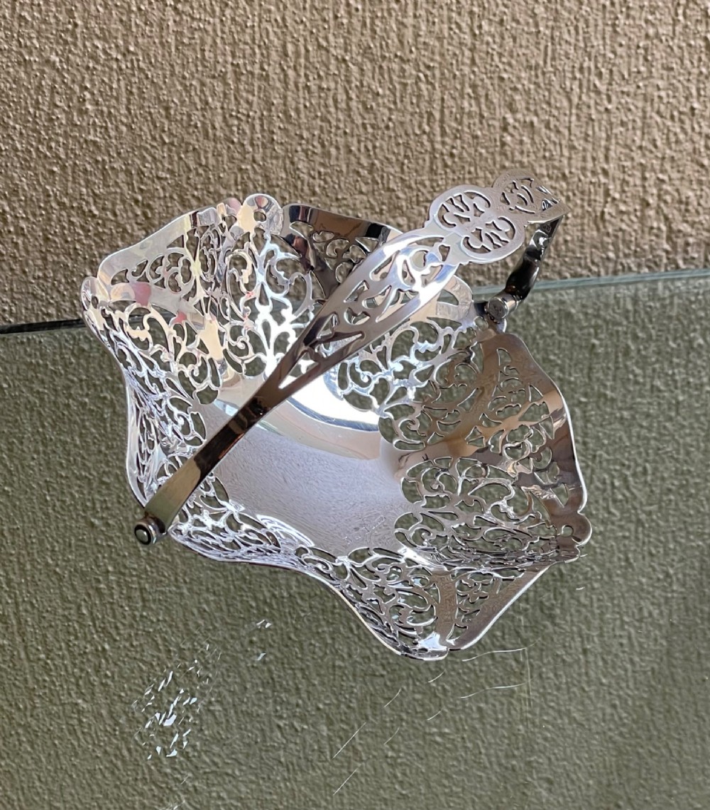 A pierced silver bonbon dish featuring a hinged overhead swing handle and intricate floral lattice openwork. View VI