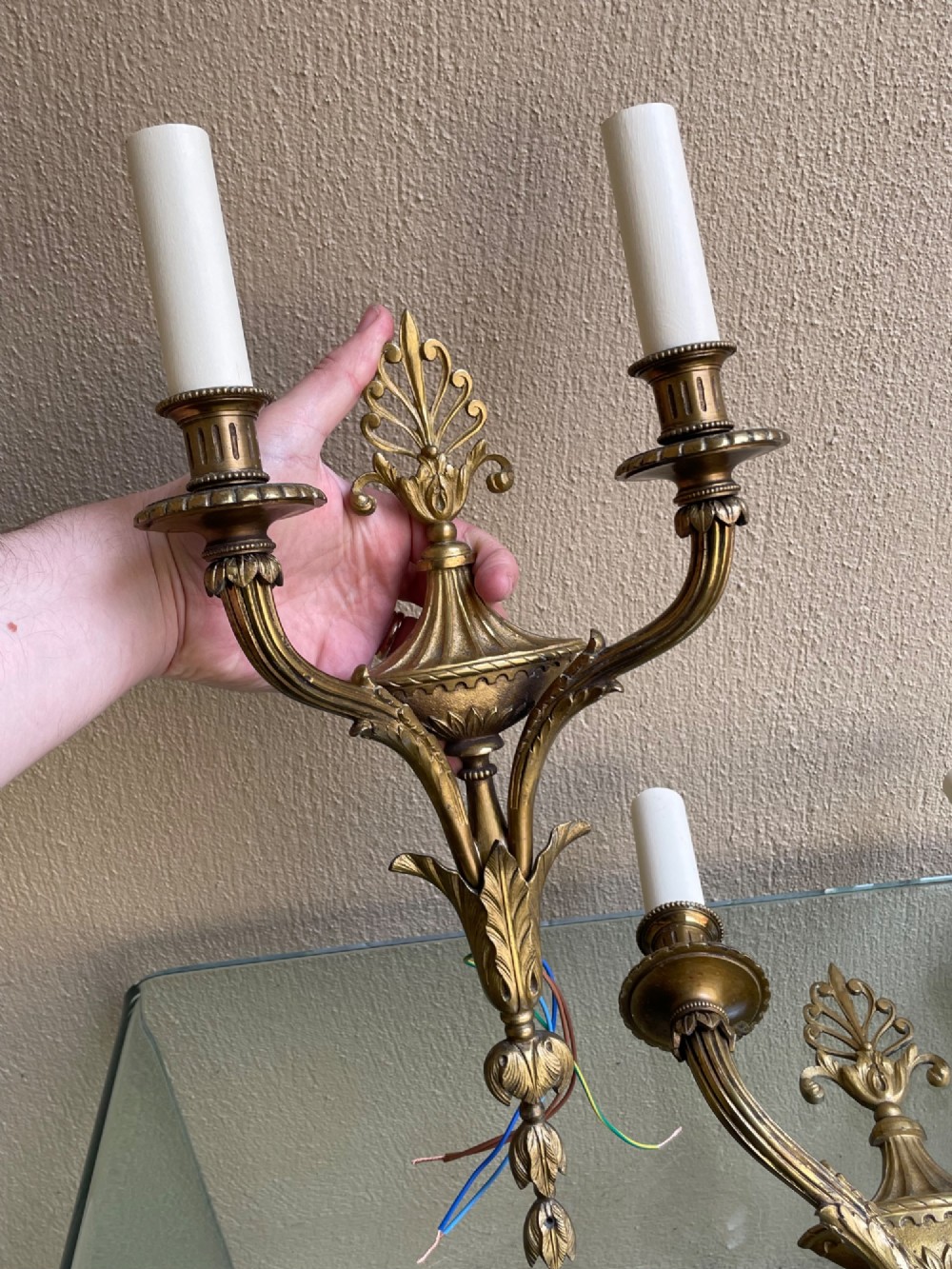 A pair of French Neoclassical gilded bronze wall sconces featuring urn-shaped central bodies, twin branches, acanthus leaf embellishments, and white candle sleeves. View V