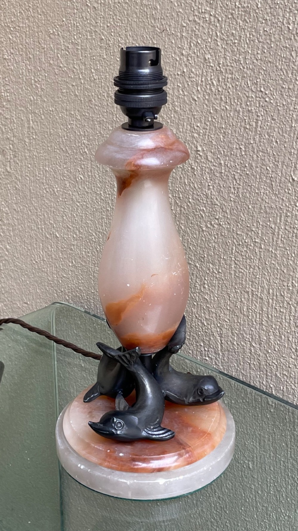 An Art Deco table lamp featuring a veined pink and cream alabaster vase column resting on three dark patinated metal dolphins over a round alabaster base. View II
