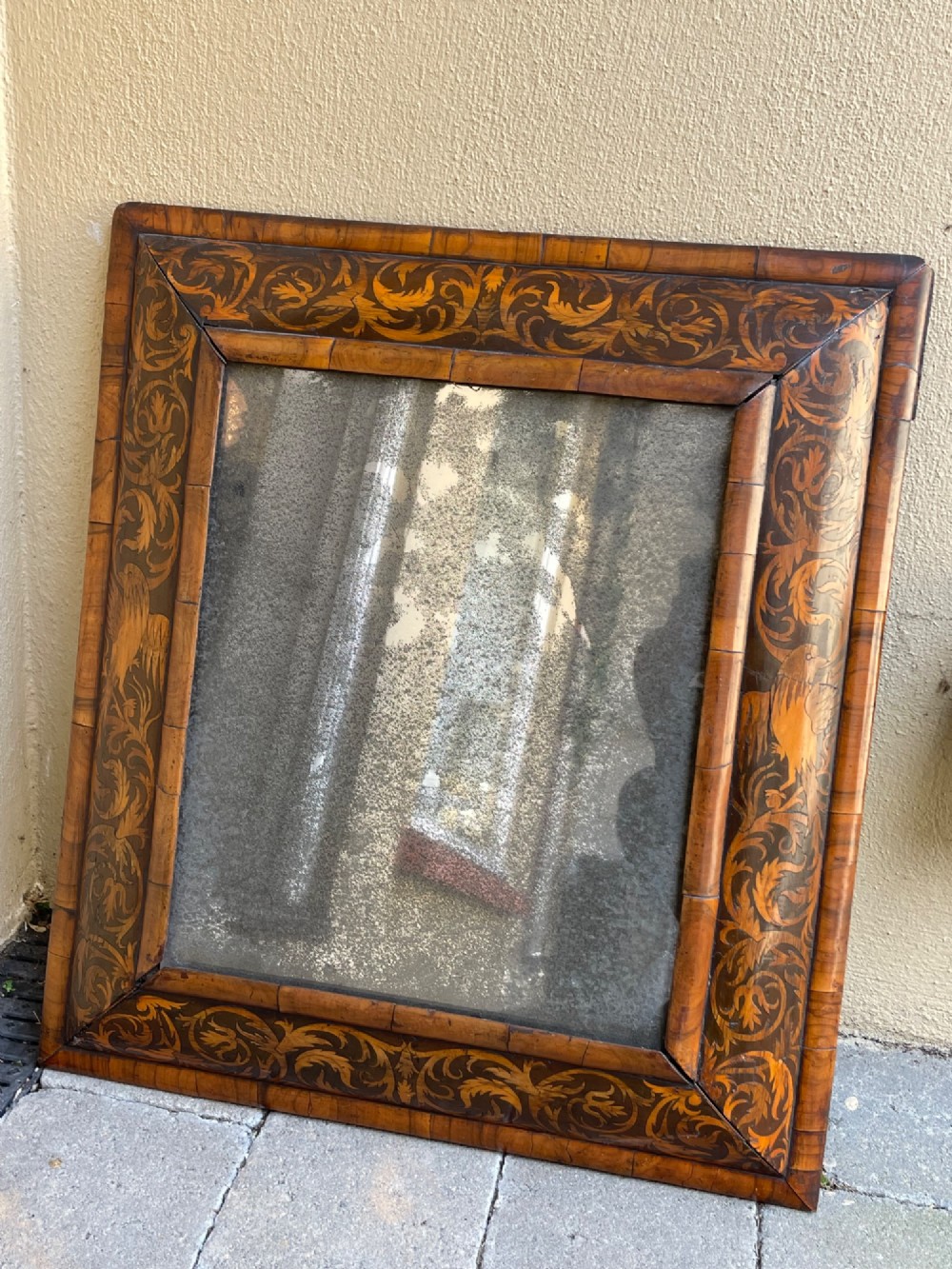 A rectangular antique William and Mary cushion-moulded wall mirror featuring intricate foliate marquetry inlay across the wooden frame and an aged glass pane.