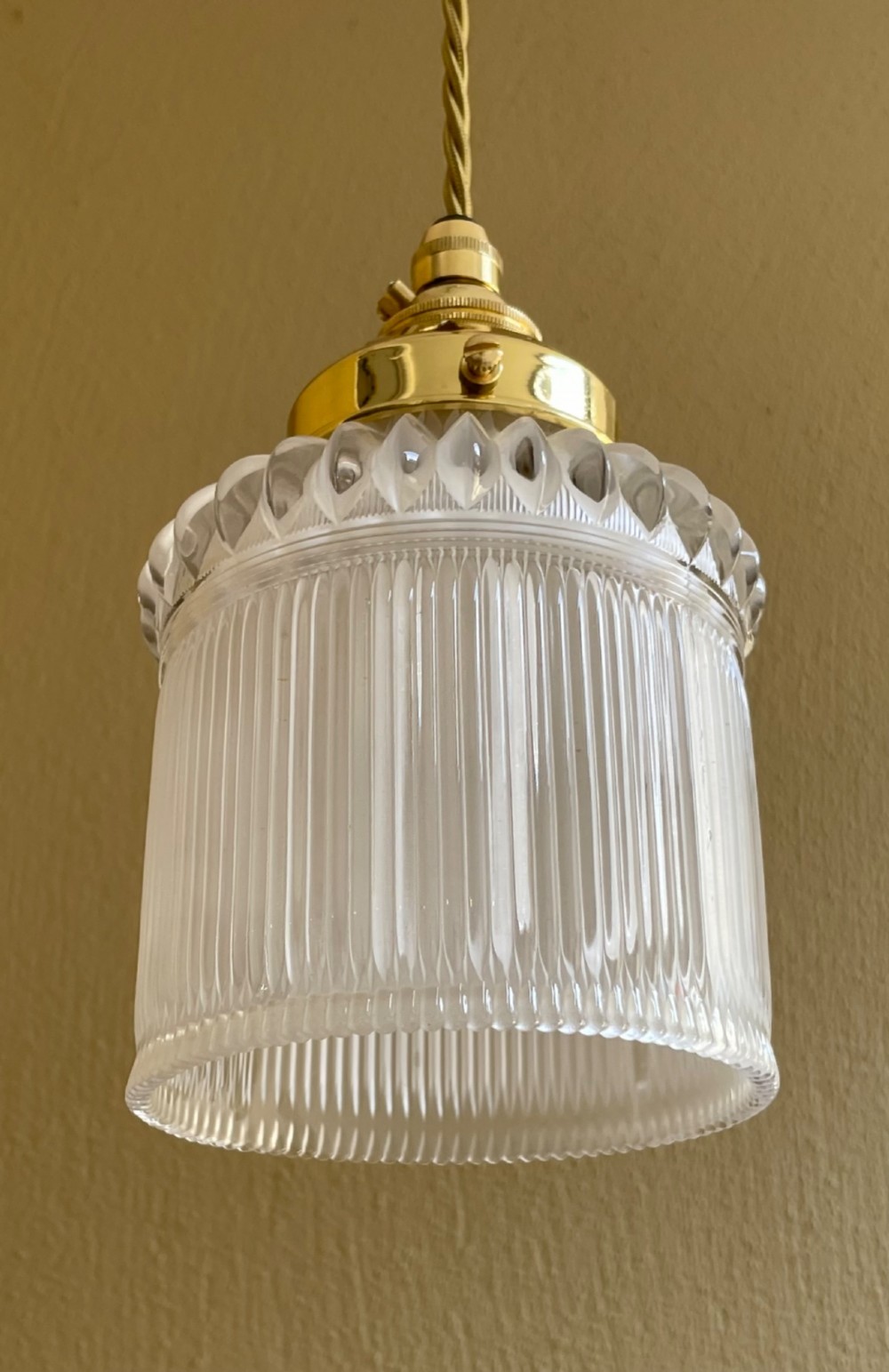 A clear ribbed Holophane glass pendant light featuring a brass gallery fitment and twisted fabric cord. View II