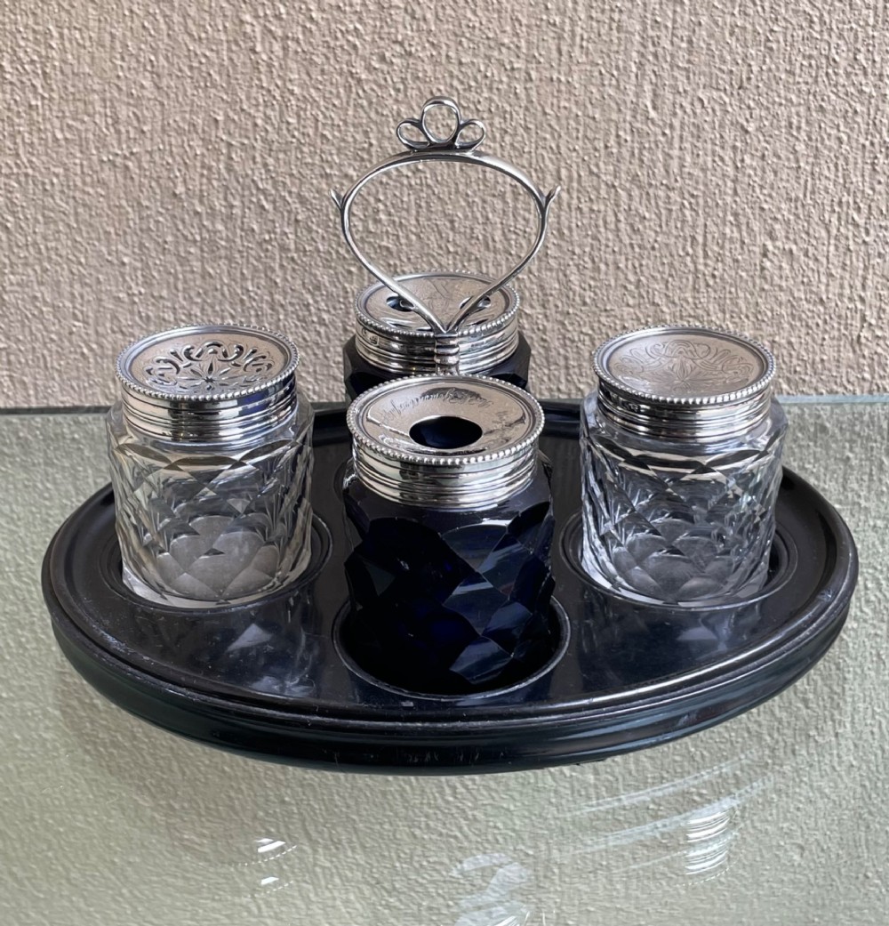 An oval ebony tray holding four diamond-cut glass pots with pierced sterling silver lids and a central silver loop handle.
