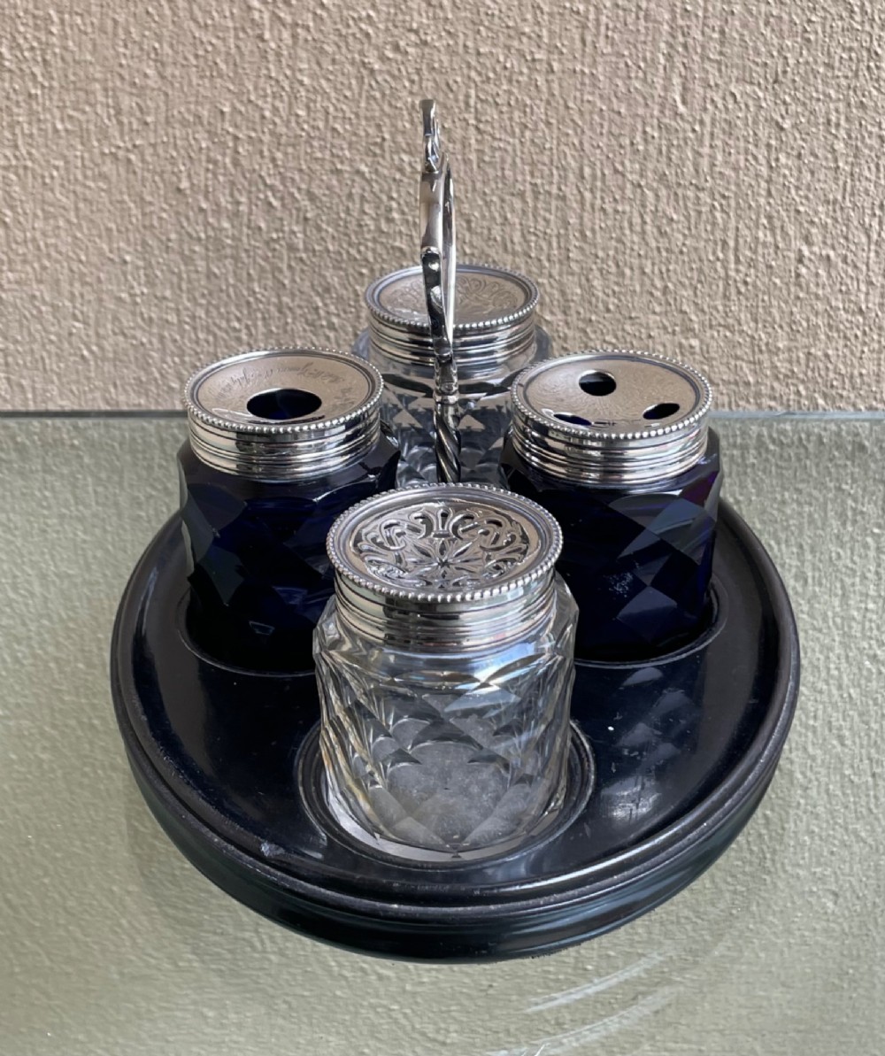 An oval ebony tray holding four diamond-cut glass pots with pierced sterling silver lids and a central silver loop handle. View VI