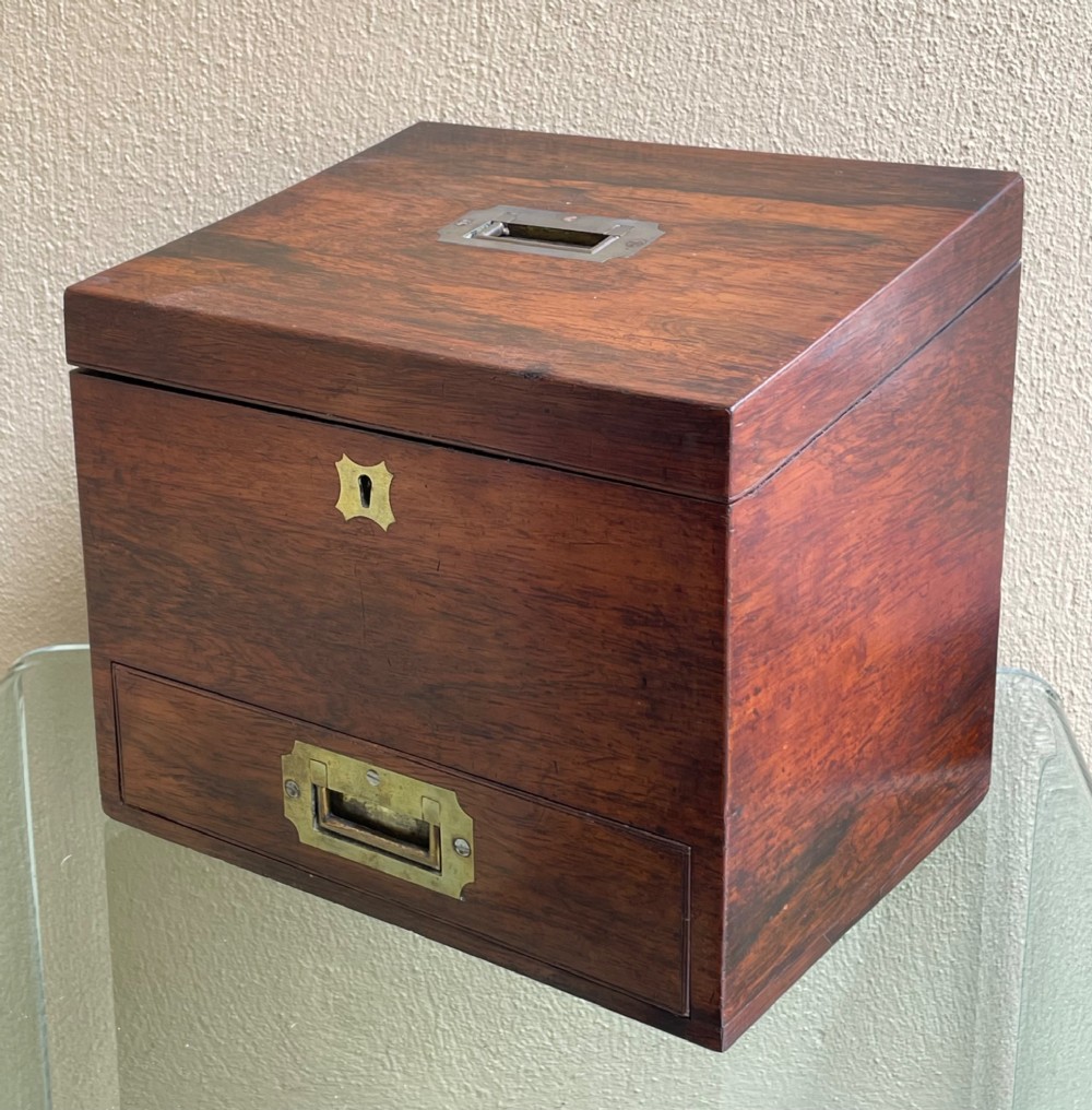 A rectangular dark wood campaign correspondence box featuring a hinged top, a brass keyhole escutcheon, and a lower drawer with a flush brass handle.
