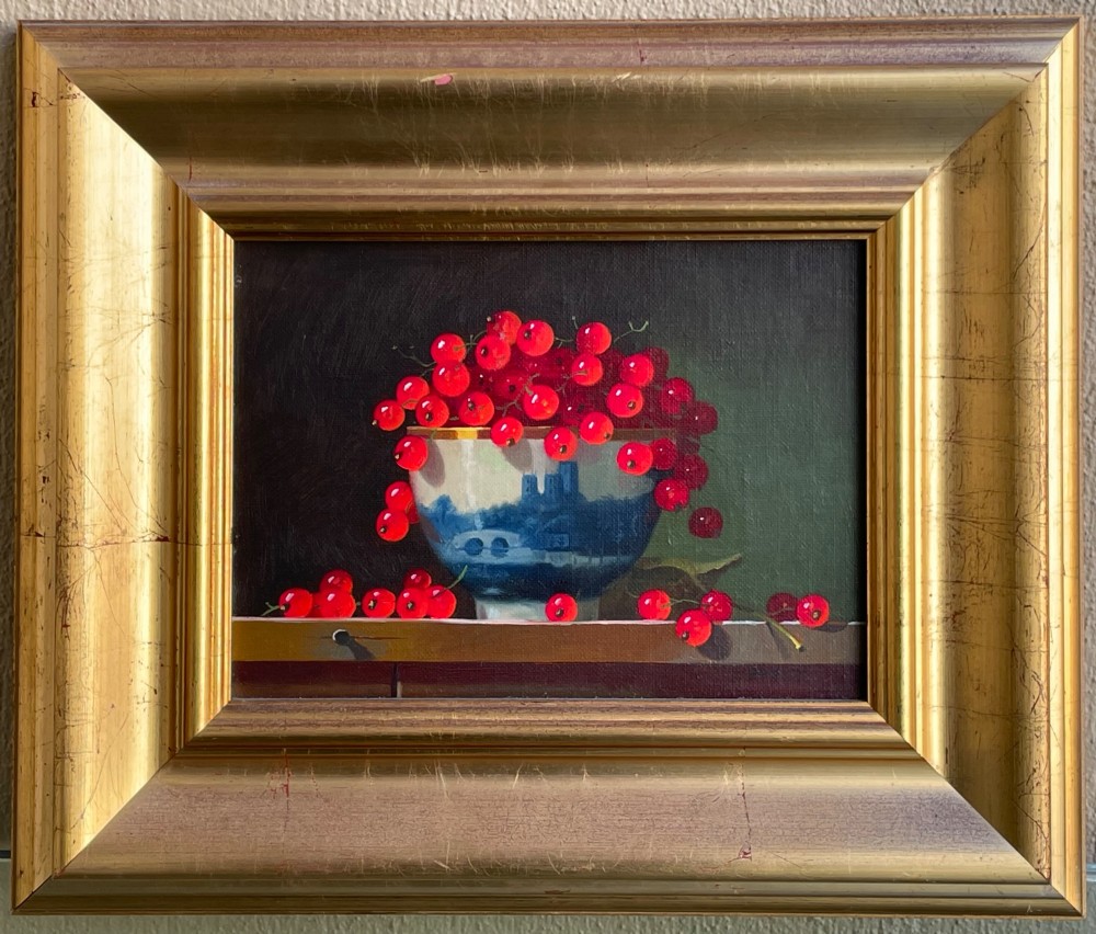 A framed oil painting depicting red berries overflowing from a blue and white porcelain bowl onto a dark wooden surface.