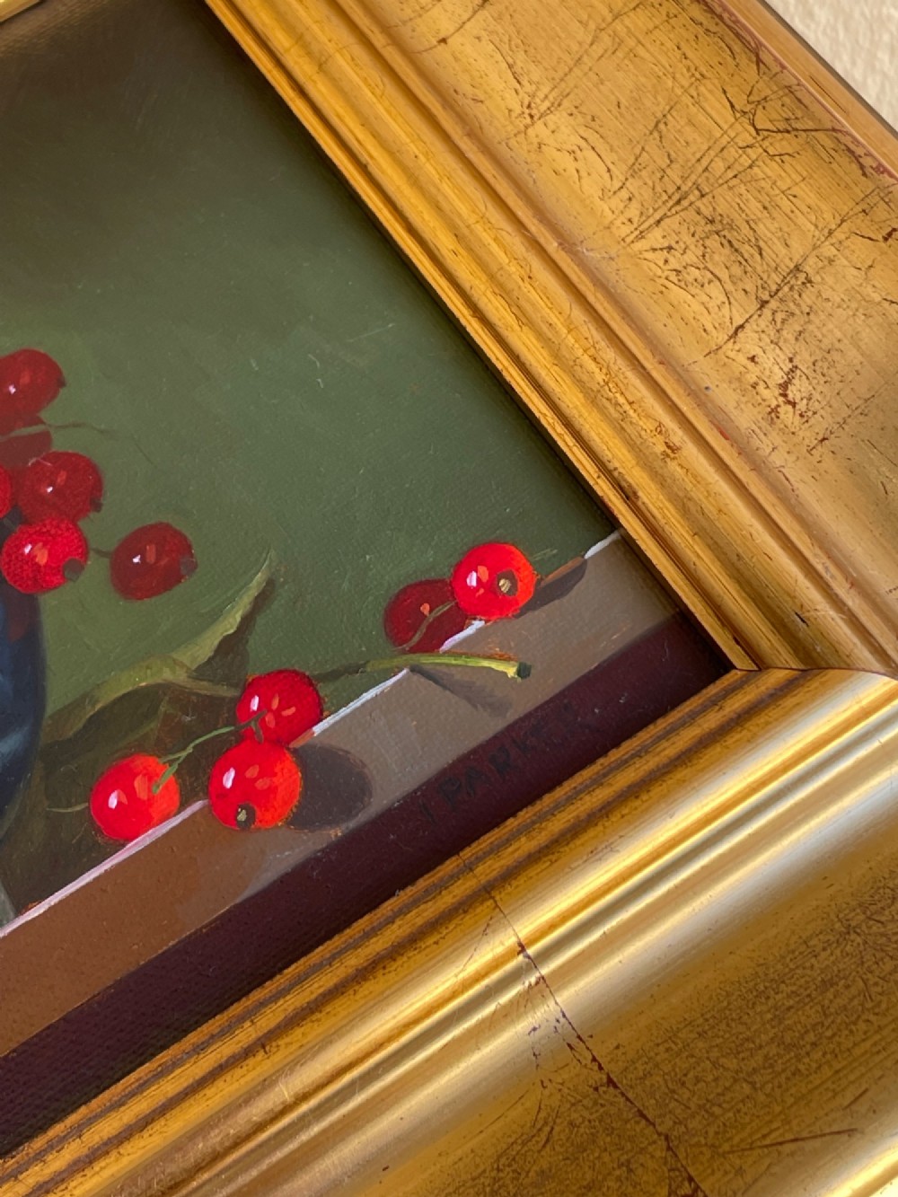 A framed oil painting depicting red berries overflowing from a blue and white porcelain bowl onto a dark wooden surface. View III