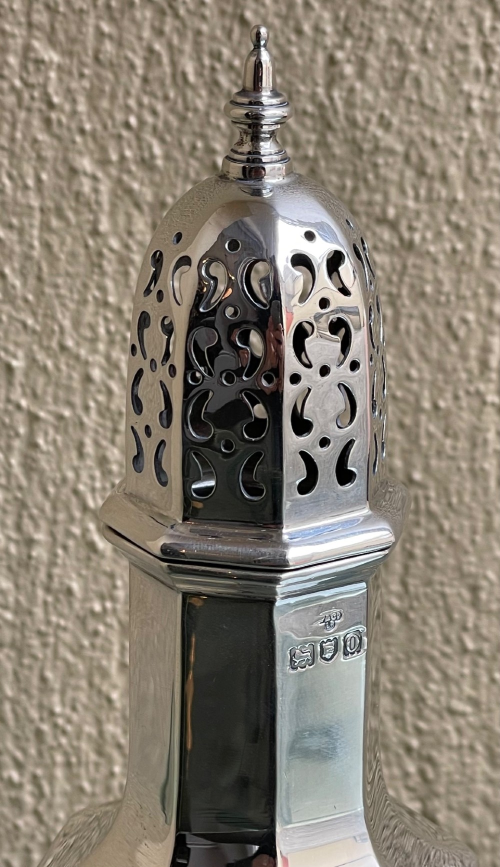 An Edwardian octagonal sterling silver sugar caster featuring a pierced domed lid topped with a finial and stamped with British hallmarks on the neck. View II