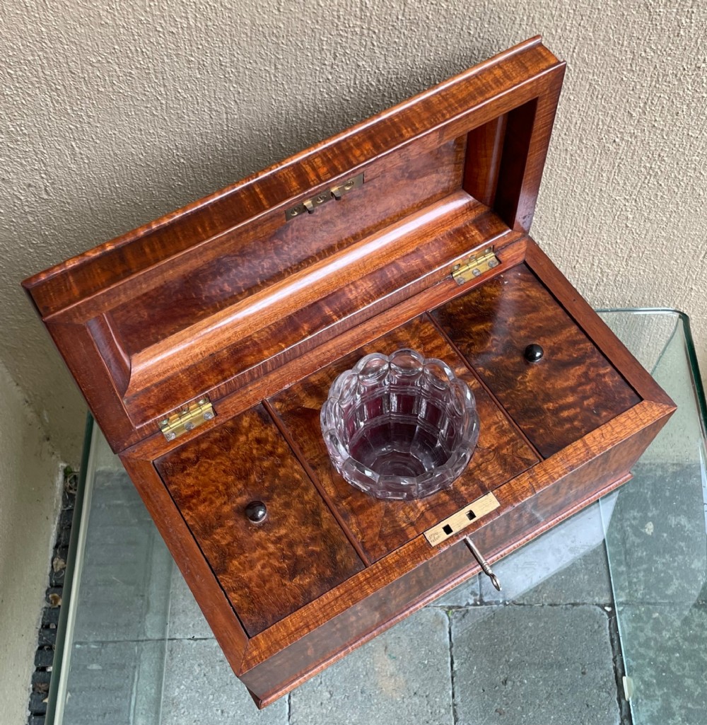 A rectangular Regency flame mahogany tea caddy featuring a stepped hinged lid and a brass key inserted into the front lock. View IV