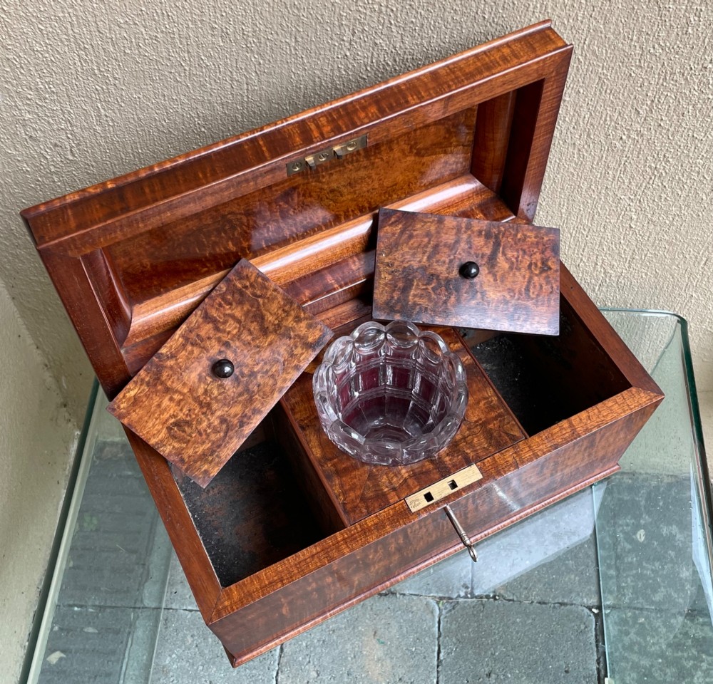 A rectangular Regency flame mahogany tea caddy featuring a stepped hinged lid and a brass key inserted into the front lock. View V