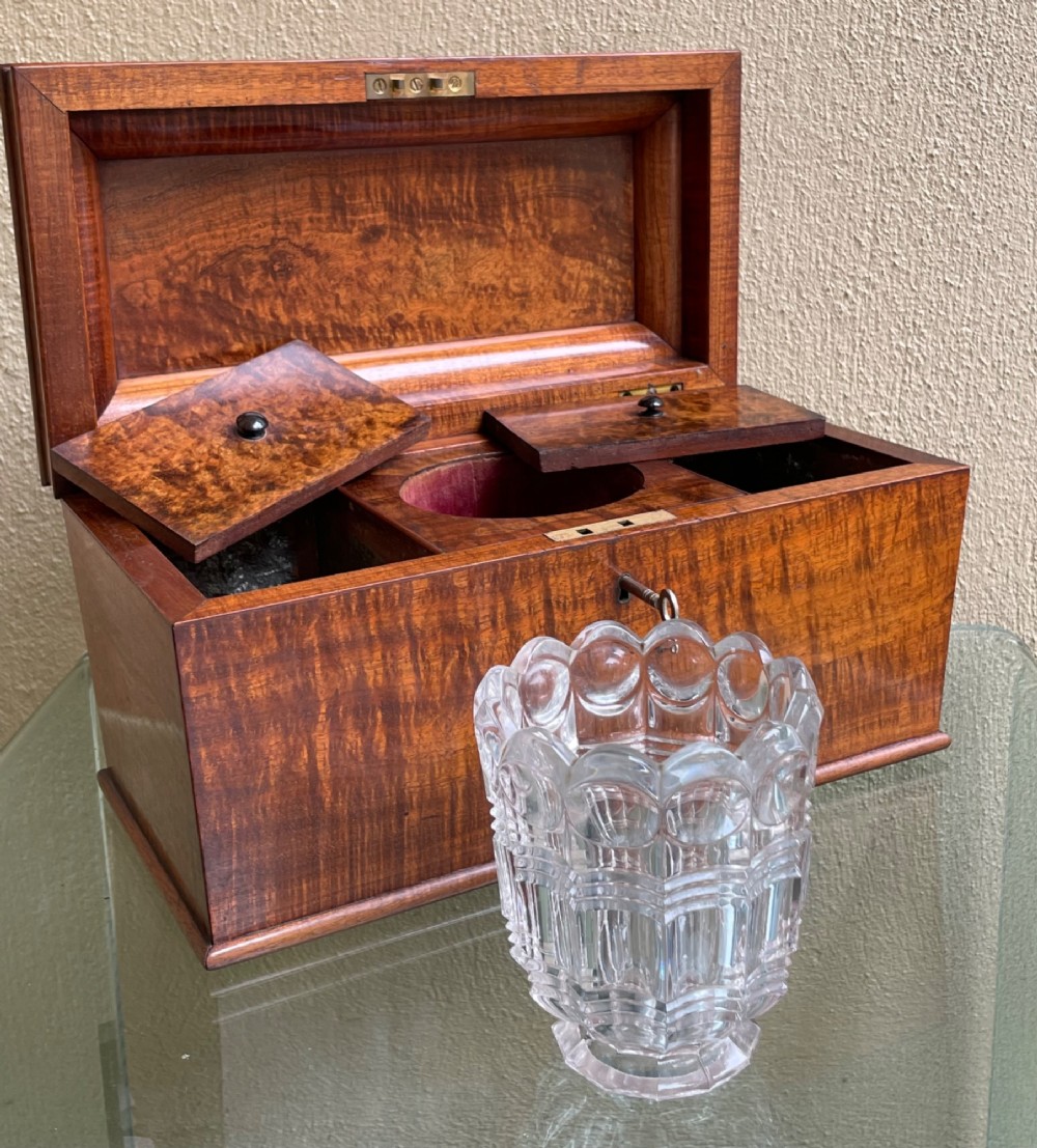 A rectangular Regency flame mahogany tea caddy featuring a stepped hinged lid and a brass key inserted into the front lock. View VI
