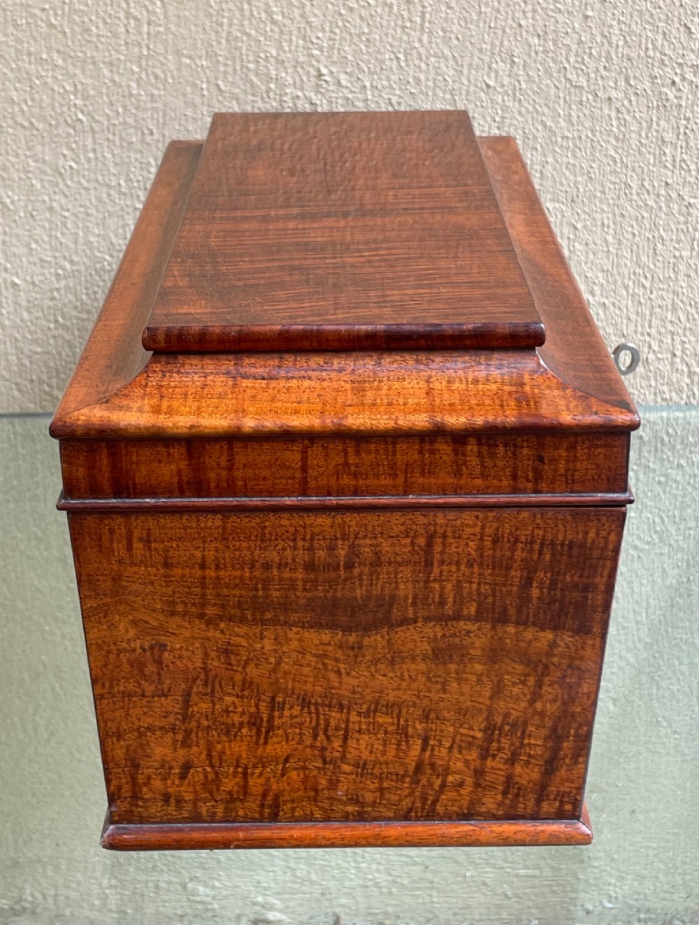 A rectangular Regency flame mahogany tea caddy featuring a stepped hinged lid and a brass key inserted into the front lock. View VII