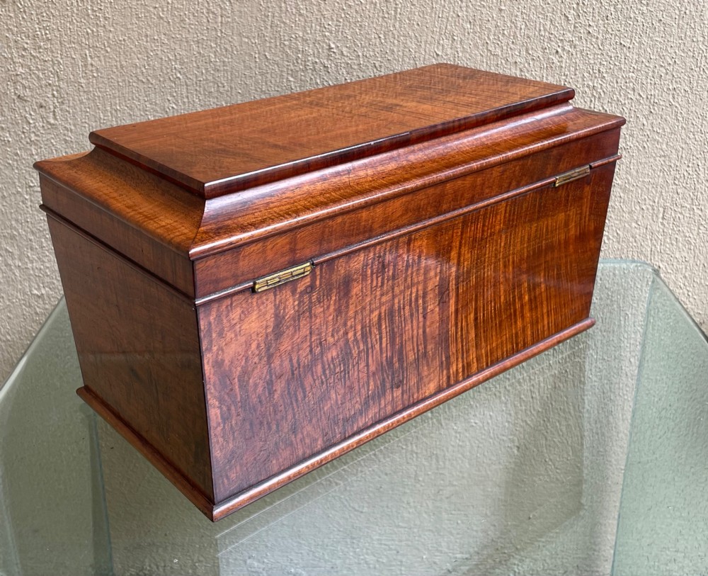 A rectangular Regency flame mahogany tea caddy featuring a stepped hinged lid and a brass key inserted into the front lock. View VIII