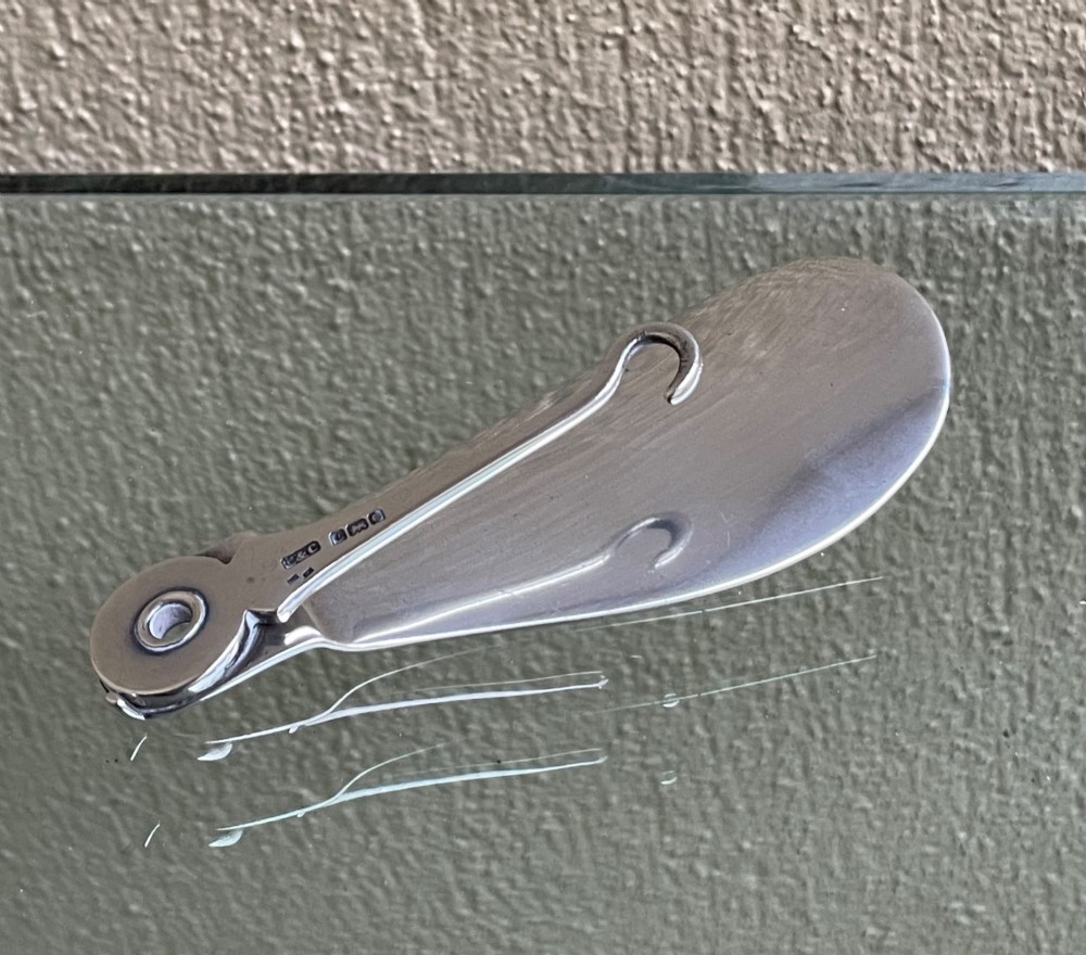 An antique sterling silver shoe horn featuring an integrated folding button hook attachment and visible British hallmarks.