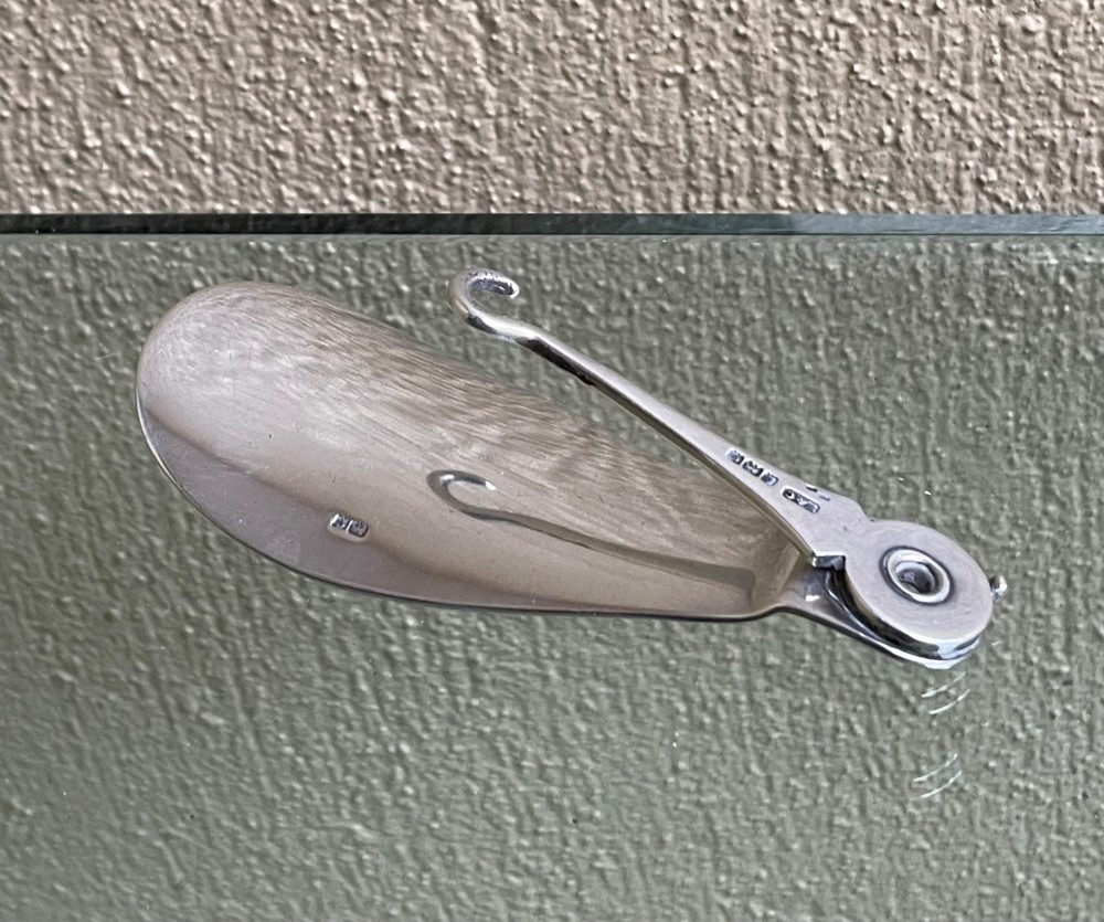 An antique sterling silver shoe horn featuring an integrated folding button hook attachment and visible British hallmarks. View II