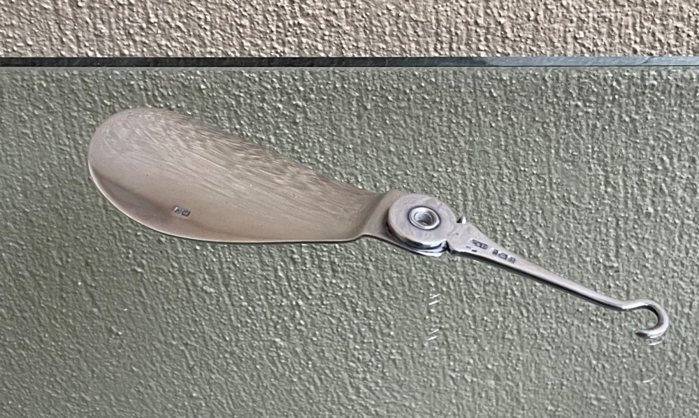 An antique sterling silver shoe horn featuring an integrated folding button hook attachment and visible British hallmarks. View III