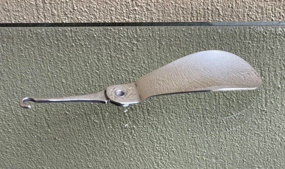 An antique sterling silver shoe horn featuring an integrated folding button hook attachment and visible British hallmarks. View V