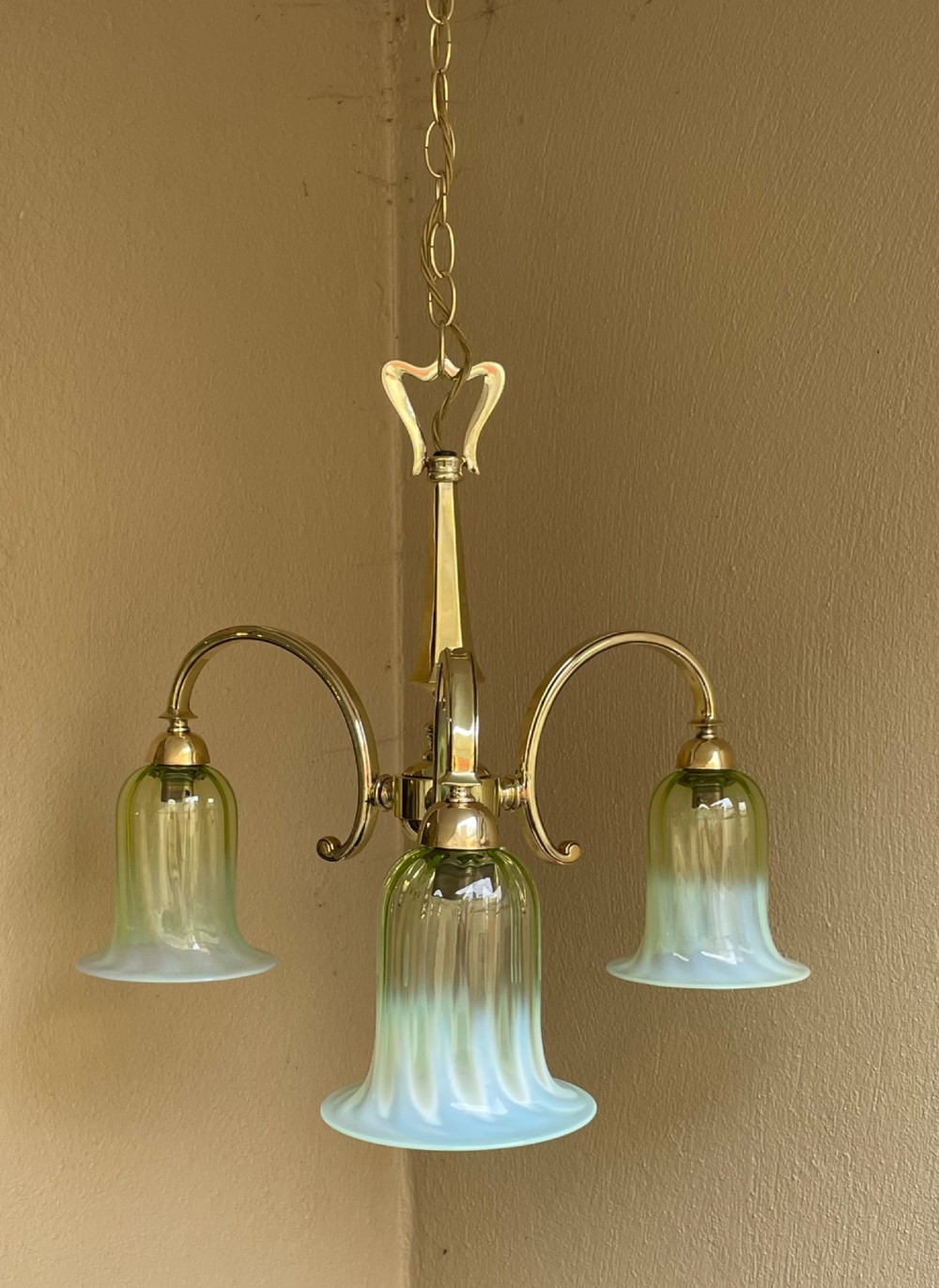 A three-arm brass chandelier with bell-shaped light green opalescent glass shades suspended from a central stem and chain. View II