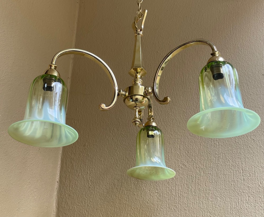 A three-arm brass chandelier with bell-shaped light green opalescent glass shades suspended from a central stem and chain. View V