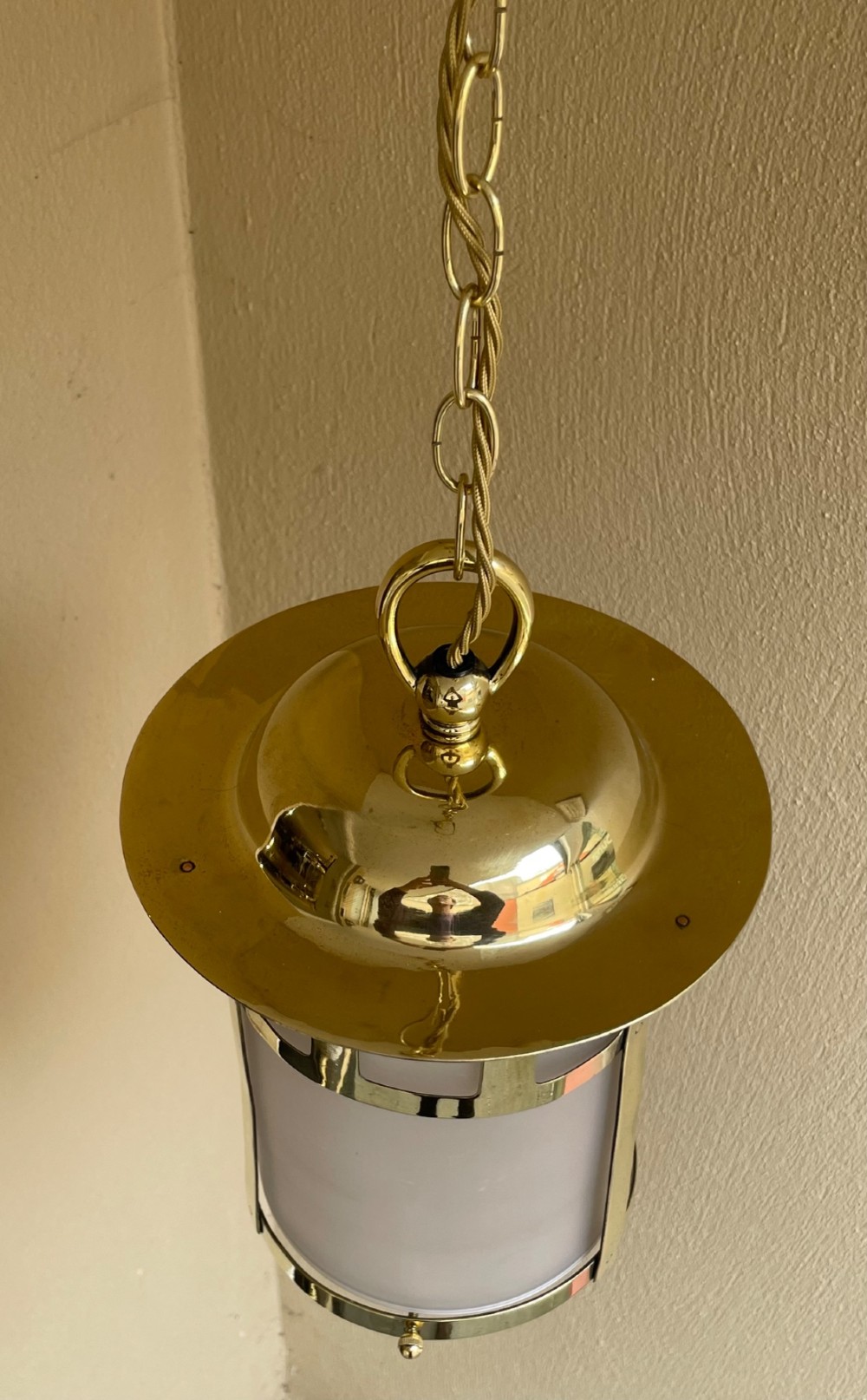 An Arts and Crafts style brass hall lantern with geometric cut-out metalwork and a frosted glass cylindrical shade, suspended by a brass chain. View VI