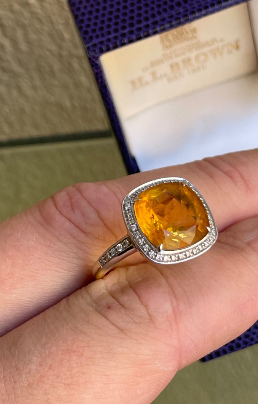 A cushion-cut yellow citrine gemstone set in a white metal ring surrounded by a border of small brilliant-cut diamonds. View II
