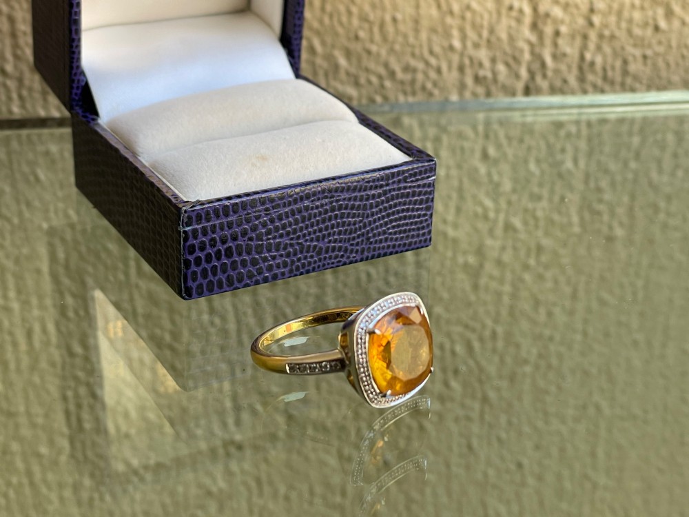 A cushion-cut yellow citrine gemstone set in a white metal ring surrounded by a border of small brilliant-cut diamonds. View III