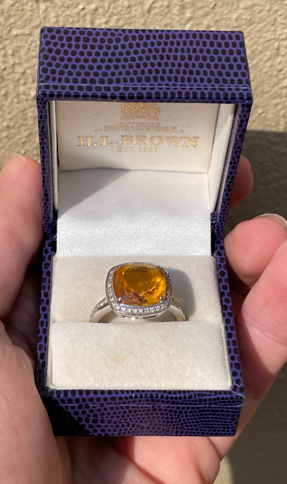 A cushion-cut yellow citrine gemstone set in a white metal ring surrounded by a border of small brilliant-cut diamonds. View IV