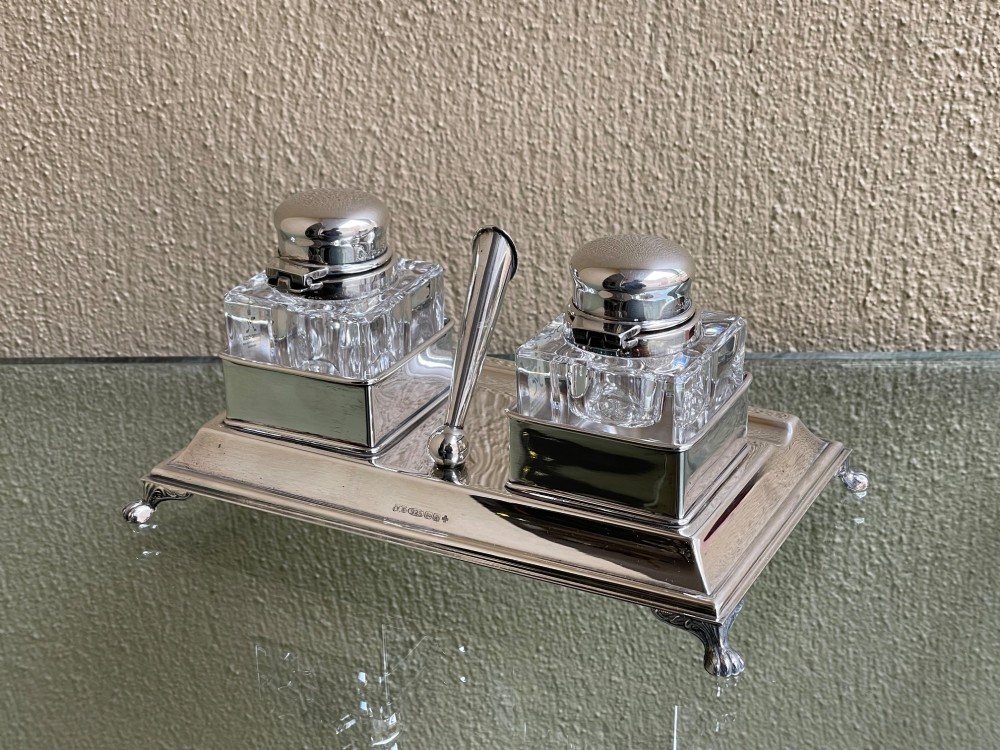 A hallmarked solid silver inkstand featuring two square cut-glass inkwells with silver lids mounted on a stepped tray with decorative feet. View IV