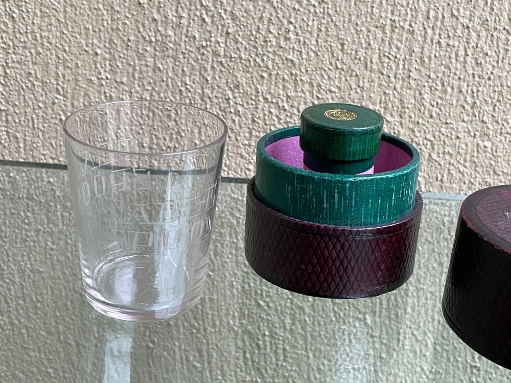A 19th-century cylindrical burgundy textured leather case with gold embossed text reading Medicine Glass and Minim Measure alongside its fitted clear glass measuring cup. View III