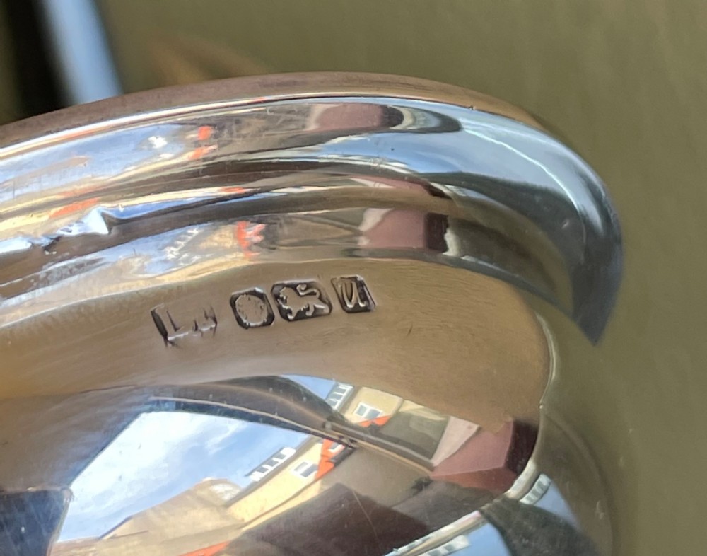 A polished sterling silver wine funnel featuring a wide rimmed bowl and a tapered curved spout resting on a flat surface. View V