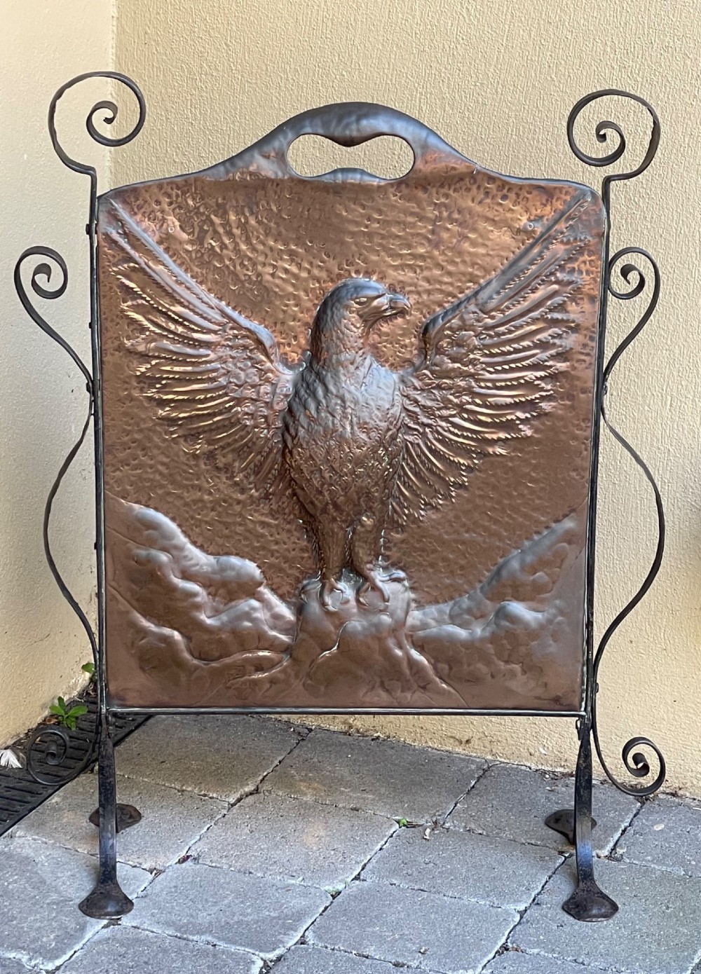 An Arts and Crafts copper fire screen featuring a hammered repousse eagle design framed by wrought iron scrollwork.