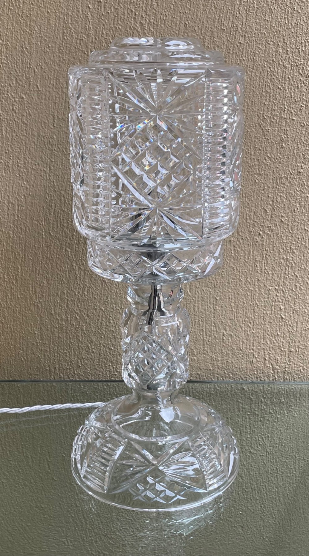 A clear cut glass table lamp featuring a cylindrical geometric shade set on a faceted glass pedestal stem and base.