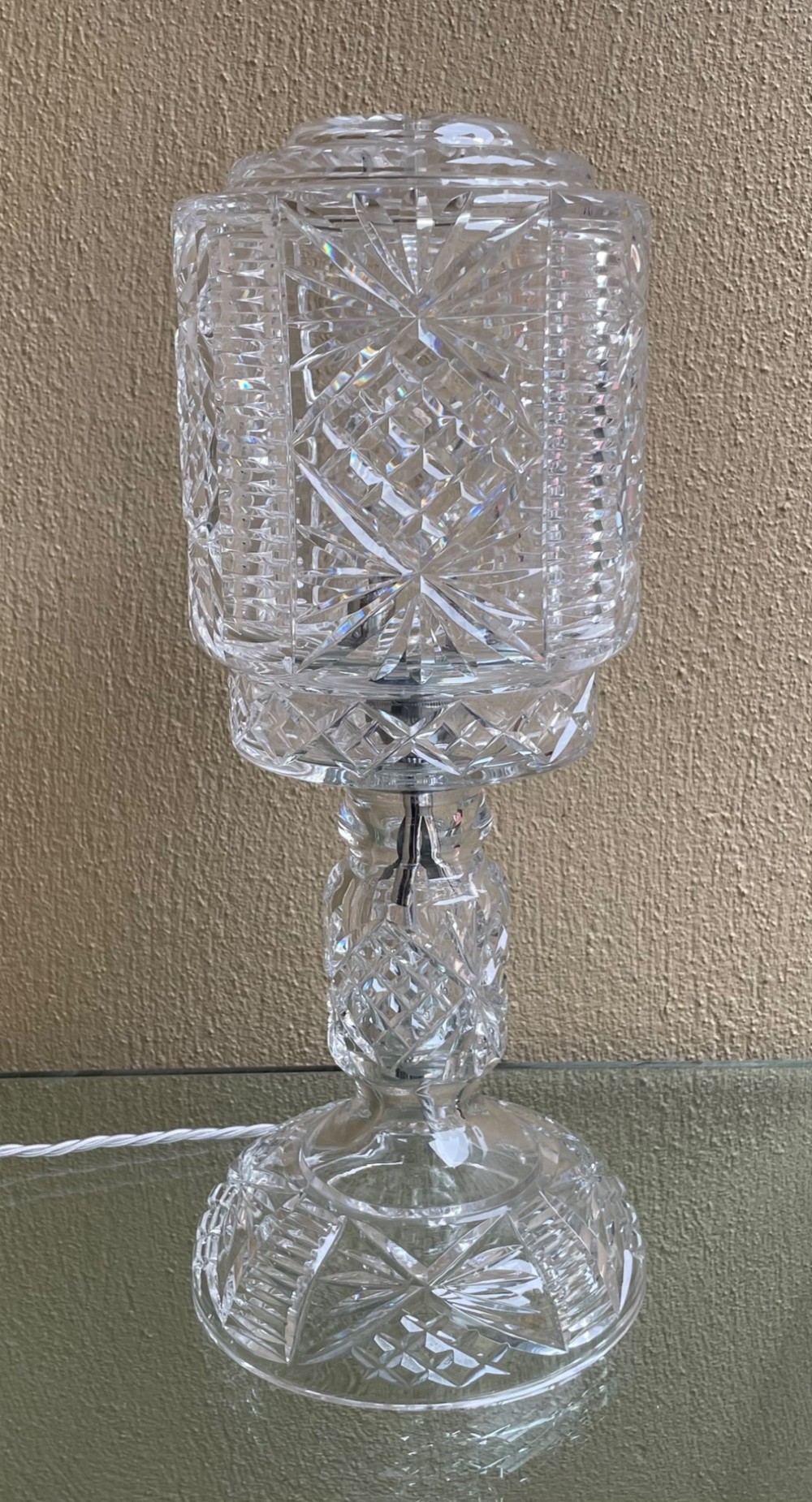 A clear cut glass table lamp featuring a cylindrical geometric shade set on a faceted glass pedestal stem and base. View III
