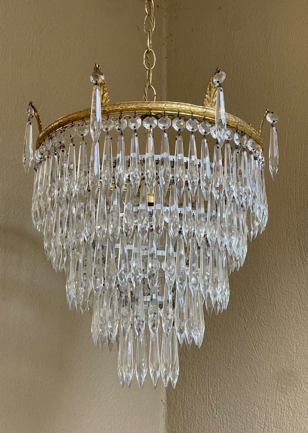 A five-tier waterfall chandelier featuring cascading rows of clear crystal drops suspended from a decorative circular brass frame. View II