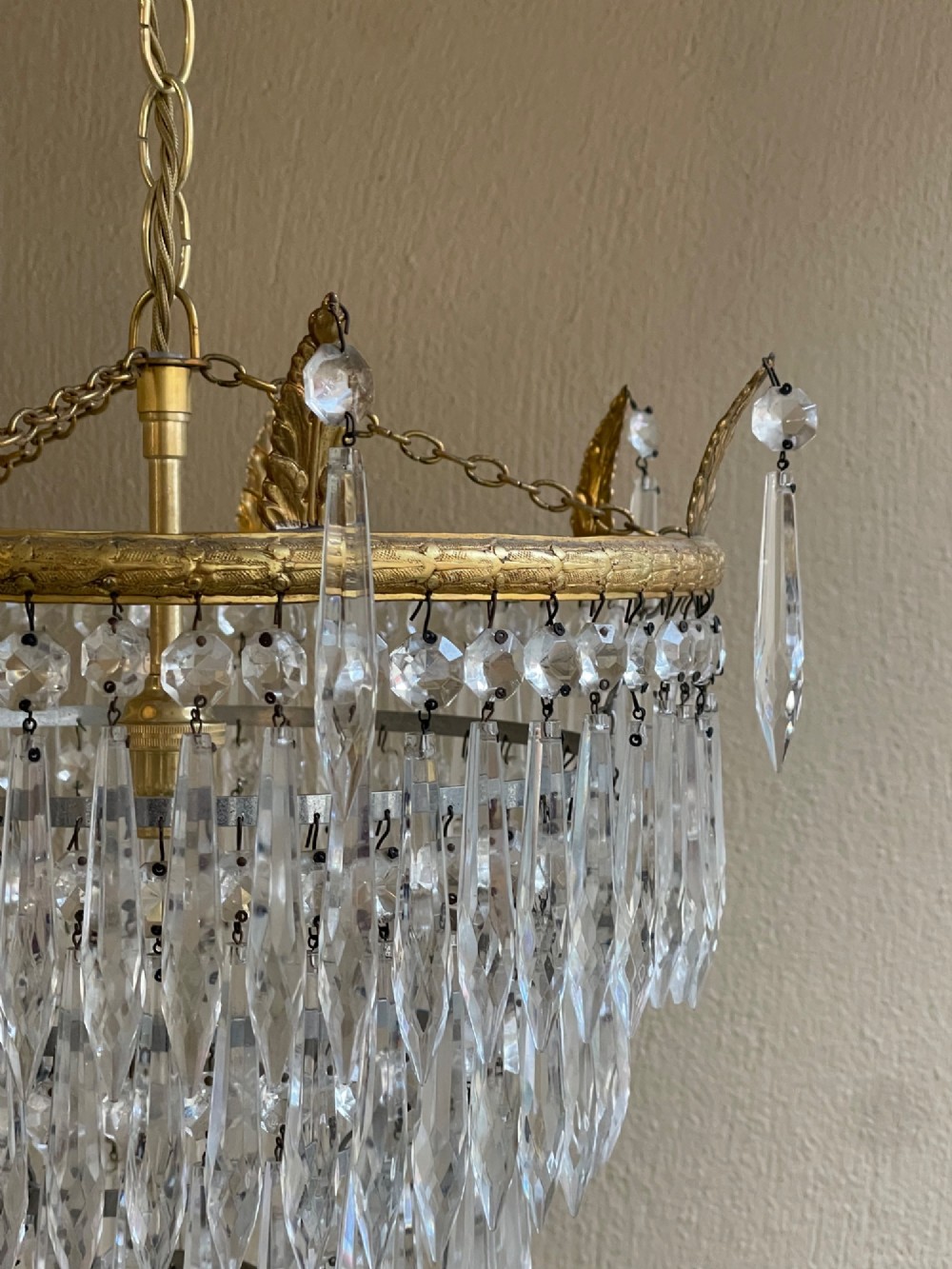 A five-tier waterfall chandelier featuring cascading rows of clear crystal drops suspended from a decorative circular brass frame. View III