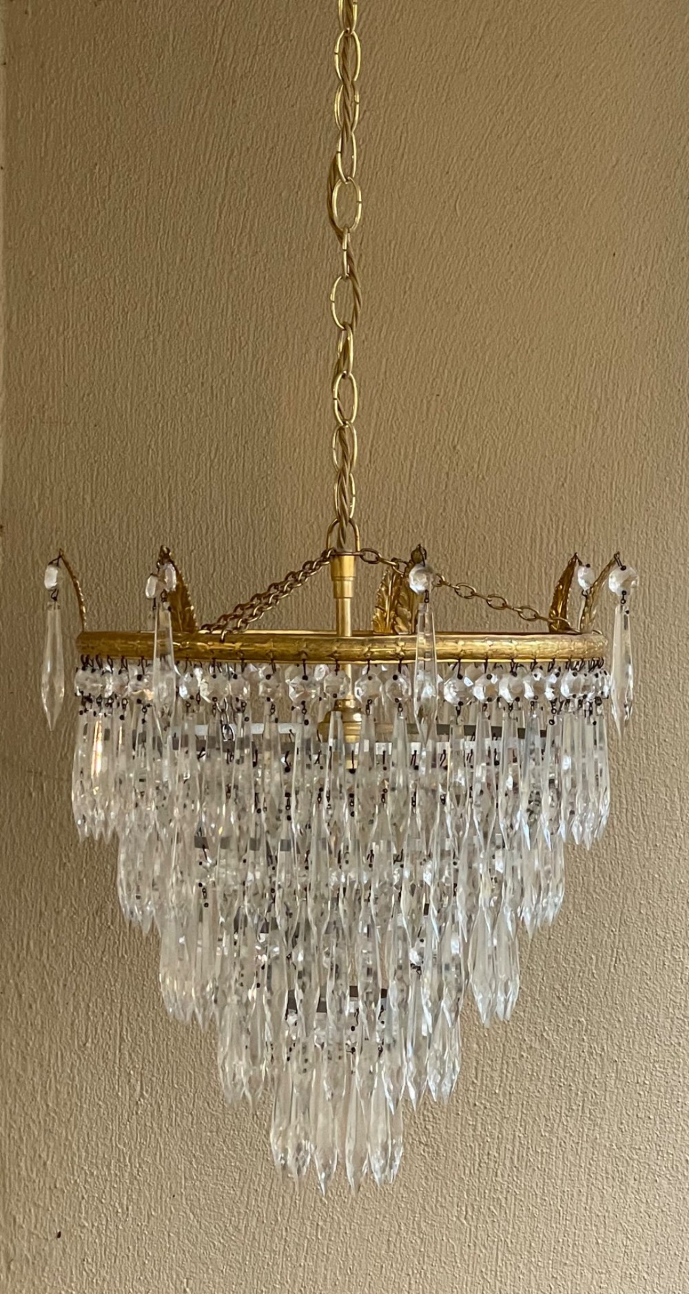 A five-tier waterfall chandelier featuring cascading rows of clear crystal drops suspended from a decorative circular brass frame. View IV