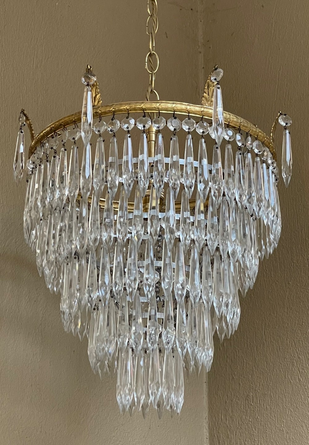 A five-tier waterfall chandelier featuring cascading rows of clear crystal drops suspended from a decorative circular brass frame. View V