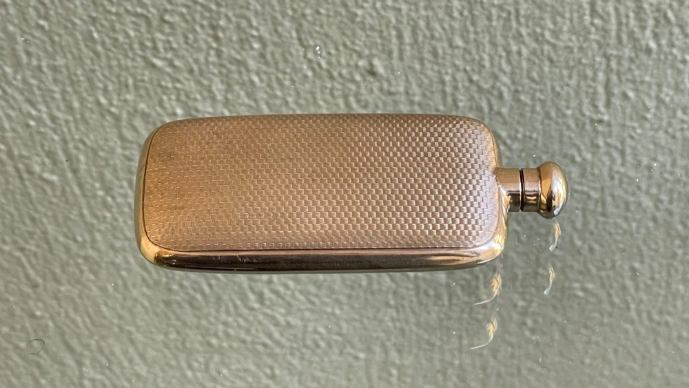 A small rectangular 9ct yellow gold scent flask featuring fine engine-turned geometric detailing, a central circular cartouche, and a screw top. View V
