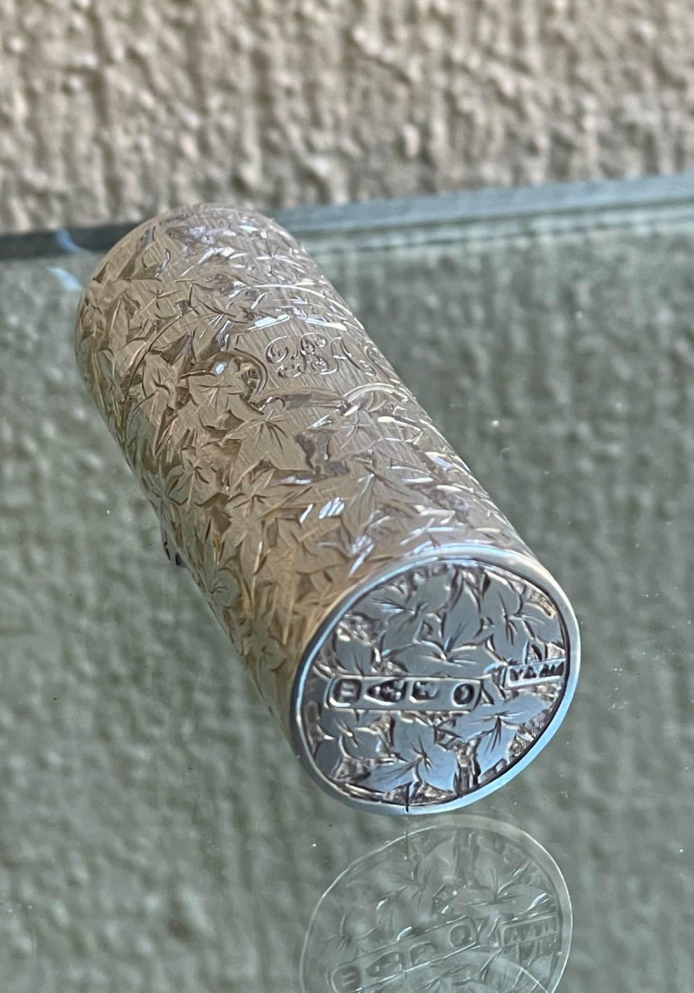 A cylindrical Victorian sterling silver scent bottle featuring chased foliage pattern work, resting inside an open leather presentation box lined with blue silk and velvet. View IV