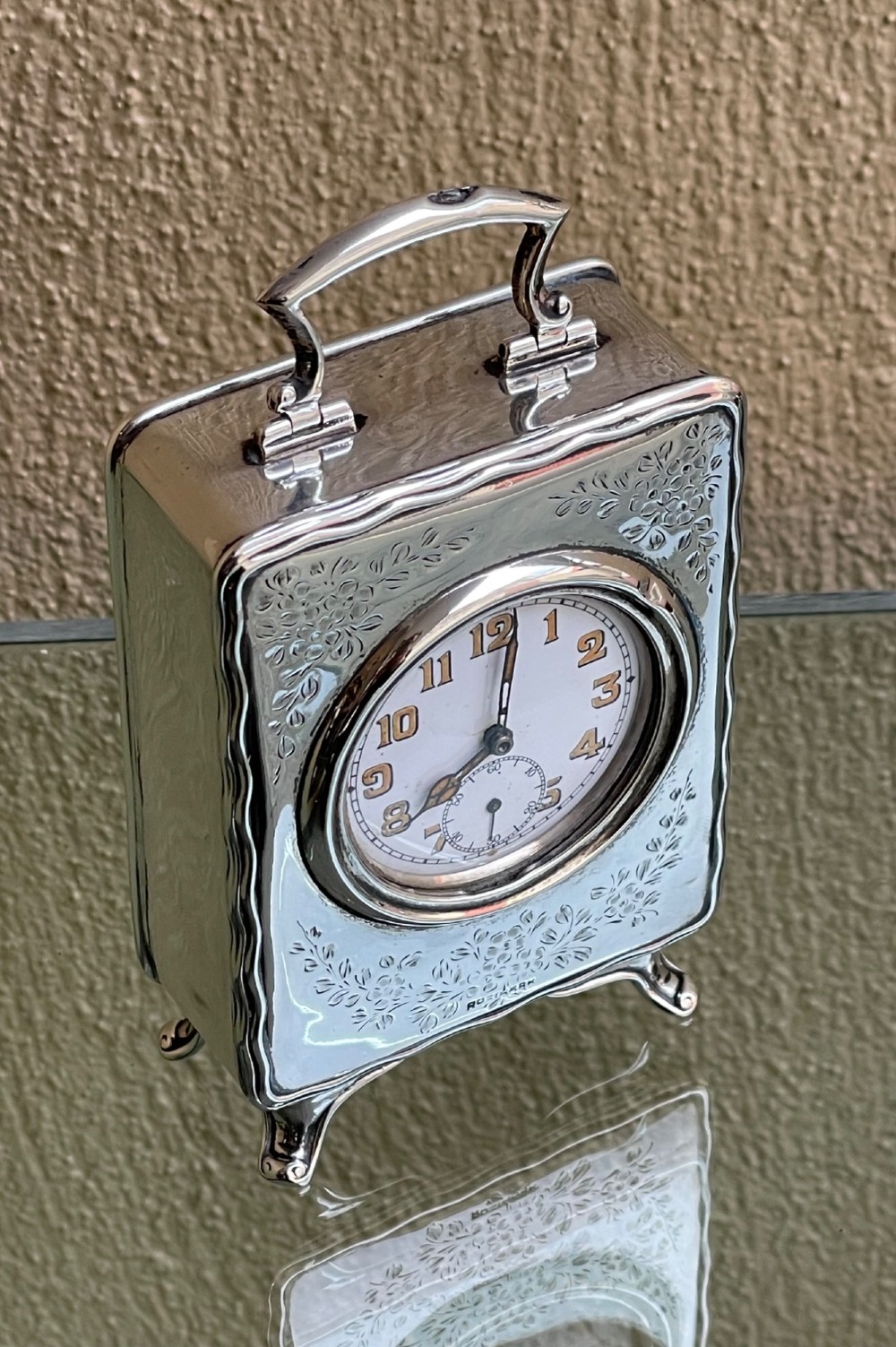 An Edwardian rectangular solid silver carriage clock featuring engraved floral foliage, a top carrying handle, cabriole feet, and a white enamel dial with Arabic numerals. View II