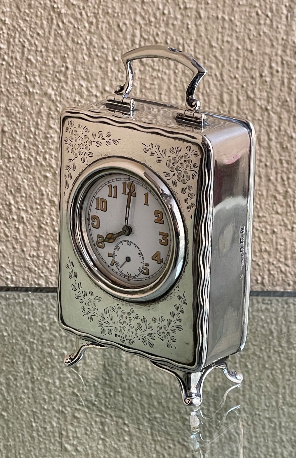 An Edwardian rectangular solid silver carriage clock featuring engraved floral foliage, a top carrying handle, cabriole feet, and a white enamel dial with Arabic numerals. View III