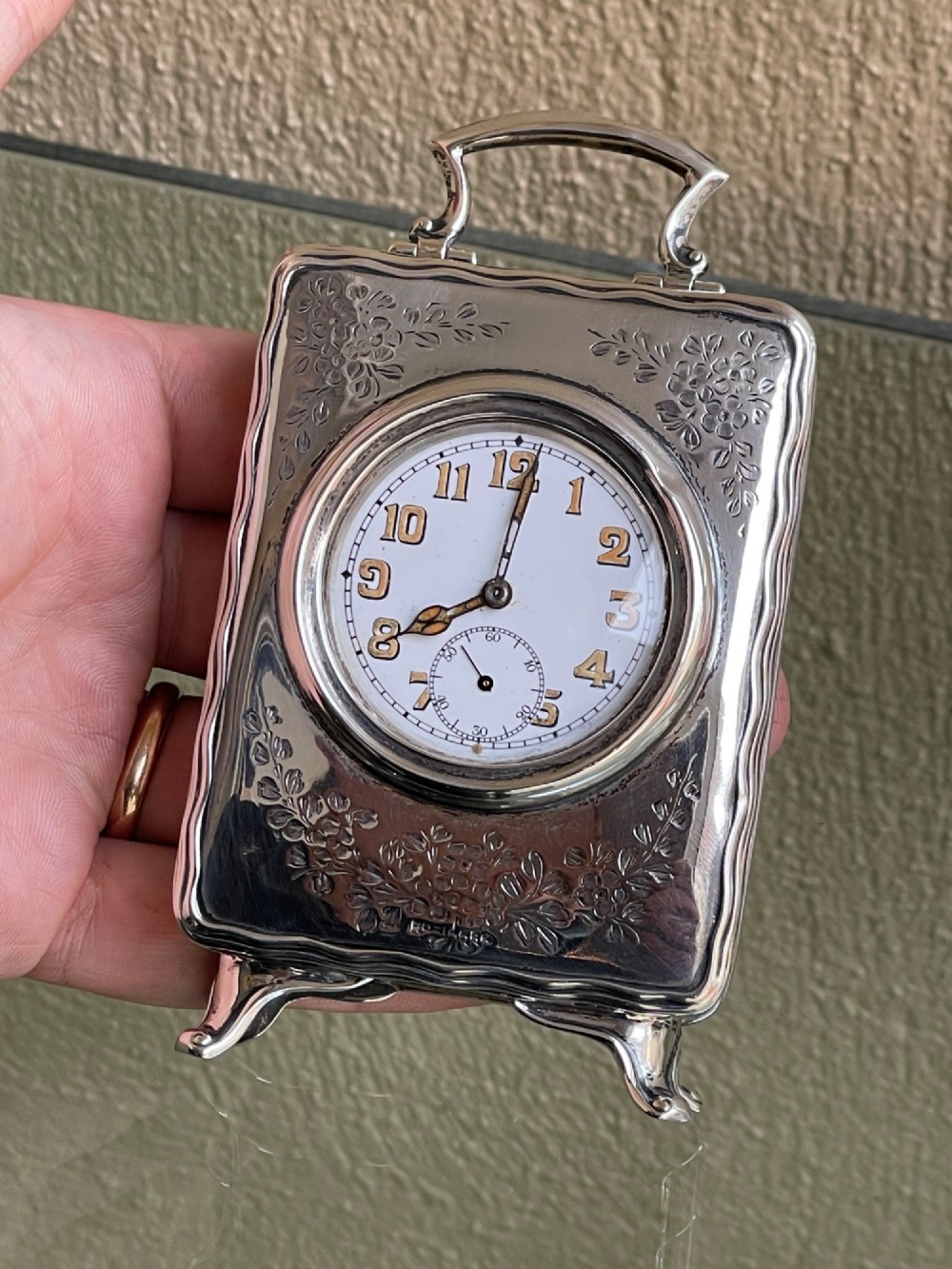 An Edwardian rectangular solid silver carriage clock featuring engraved floral foliage, a top carrying handle, cabriole feet, and a white enamel dial with Arabic numerals. View IV