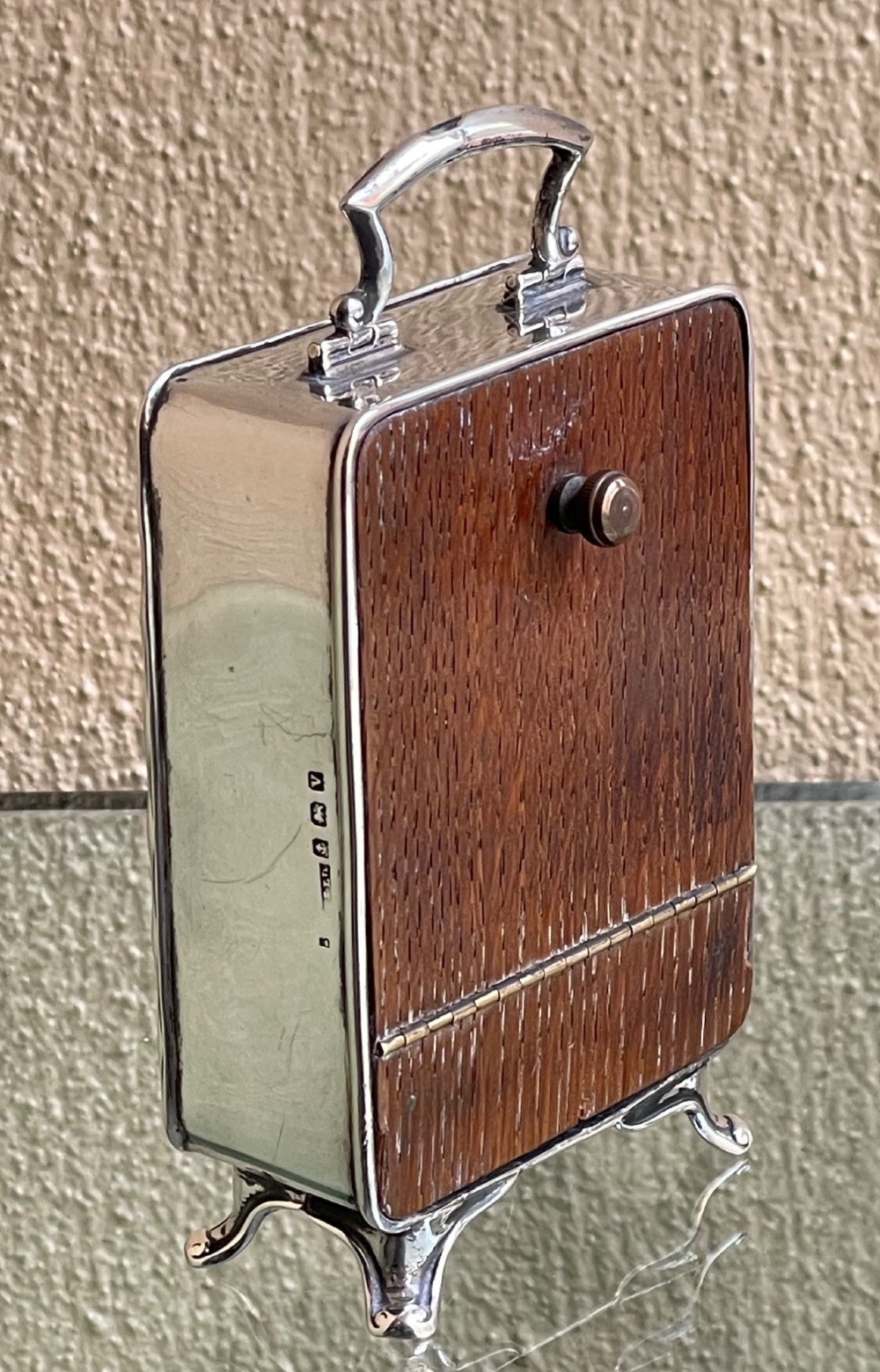 An Edwardian rectangular solid silver carriage clock featuring engraved floral foliage, a top carrying handle, cabriole feet, and a white enamel dial with Arabic numerals. View VI
