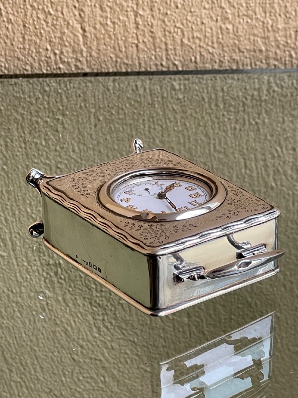 An Edwardian rectangular solid silver carriage clock featuring engraved floral foliage, a top carrying handle, cabriole feet, and a white enamel dial with Arabic numerals. View VII