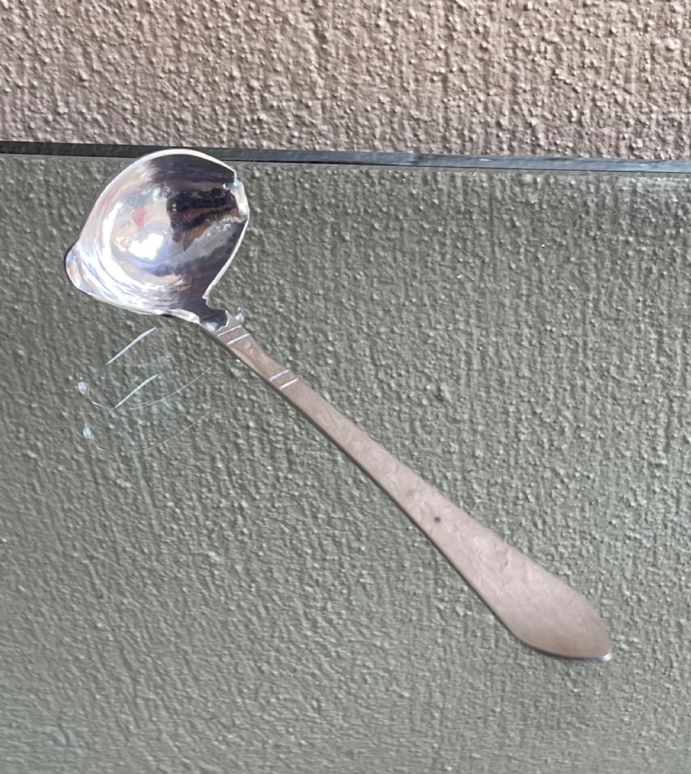 A sterling silver Georg Jensen sauce ladle with a side pouring spout and a slender handle with linear accents. View V