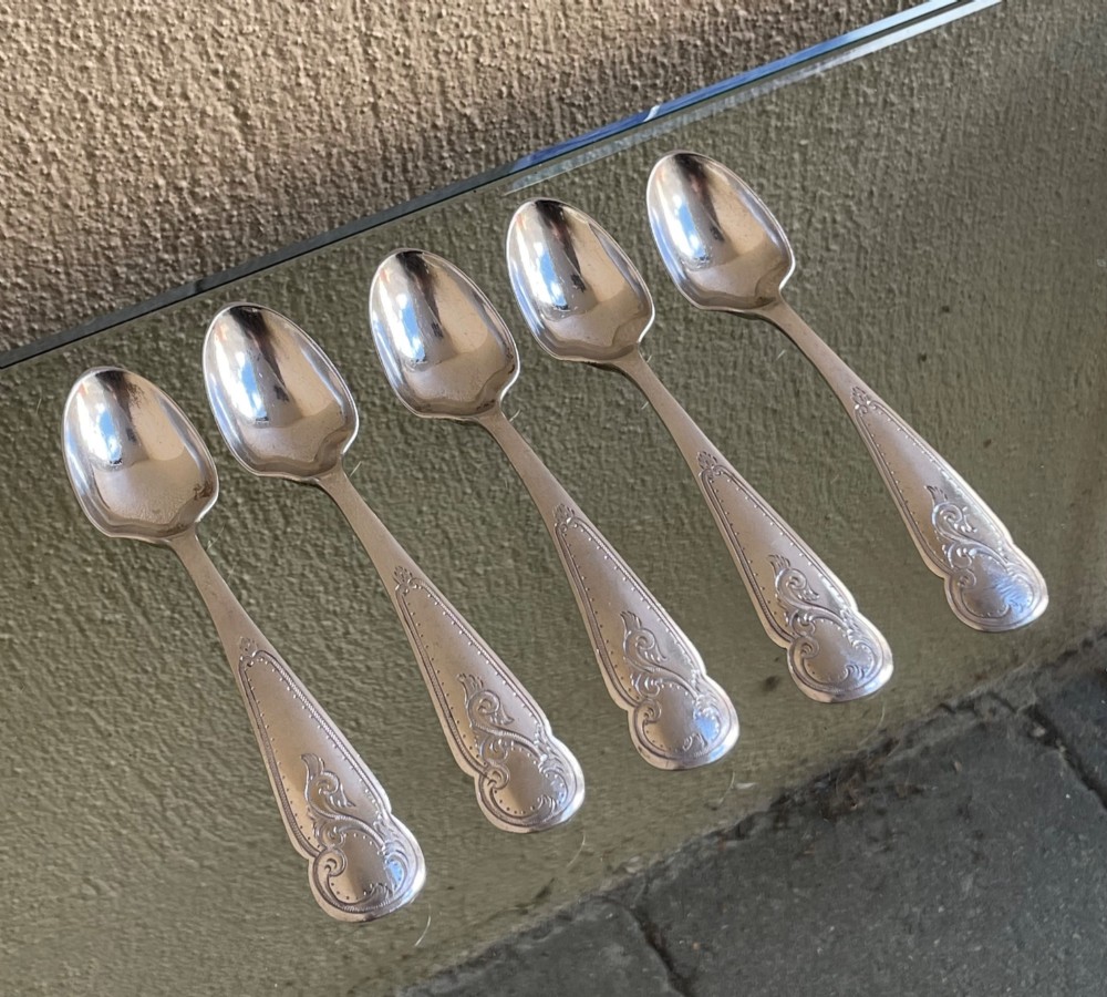 A set of five George V silver egg spoons featuring decorative engraved scrolled handles laid flat in a row. View II