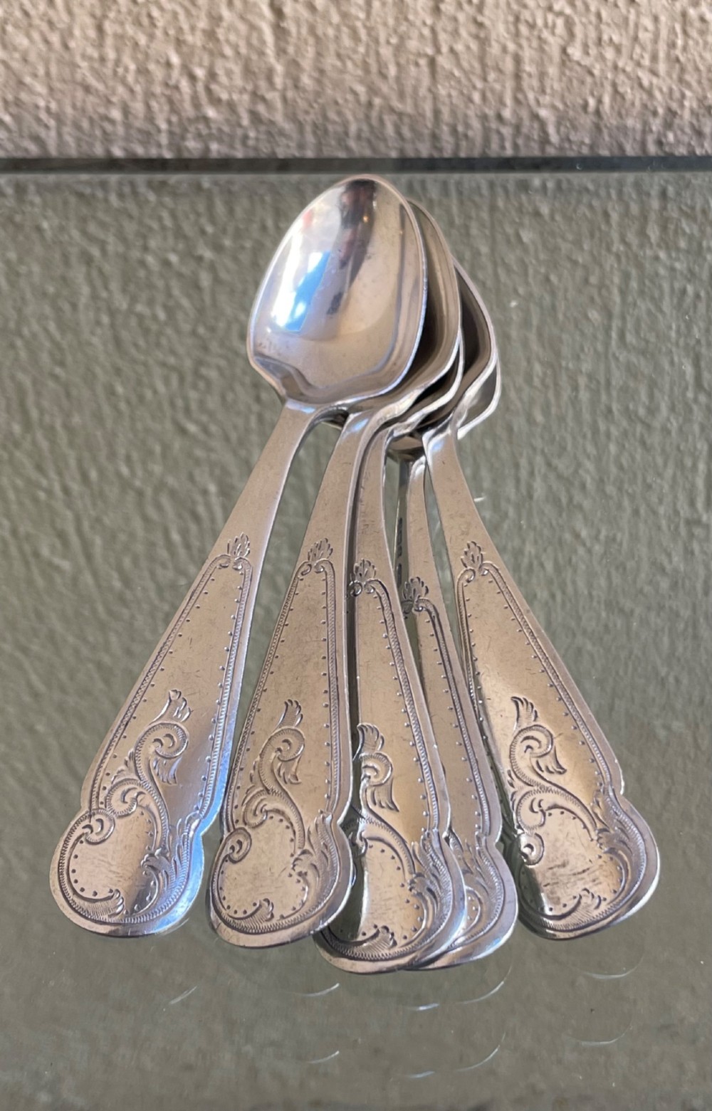 A set of five George V silver egg spoons featuring decorative engraved scrolled handles laid flat in a row. View III